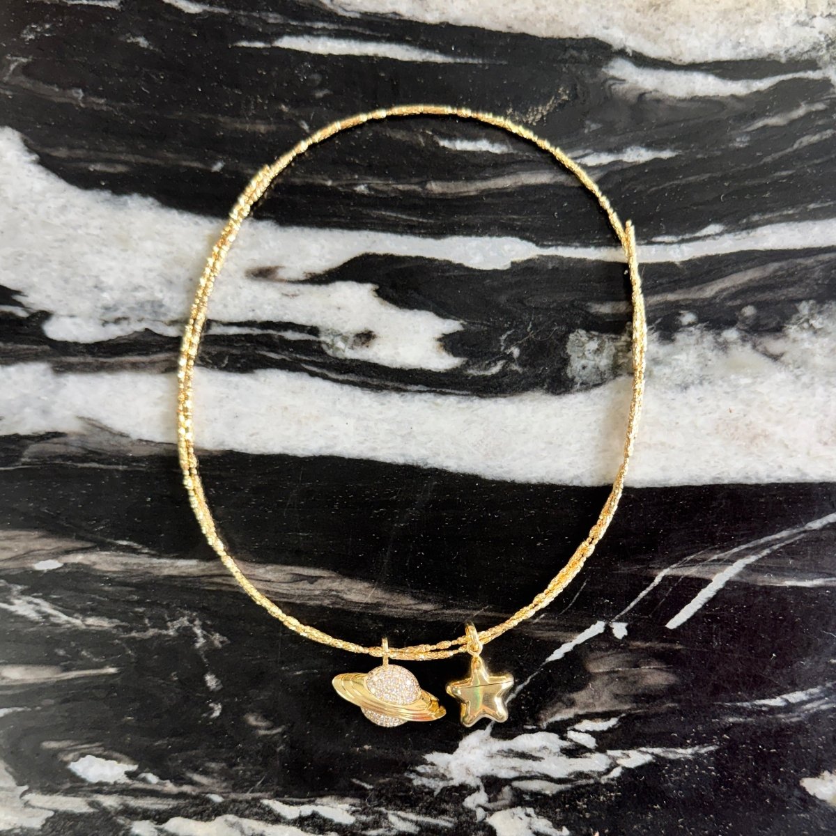 Gold necklace with star and leaf charms on a black and white marble surface