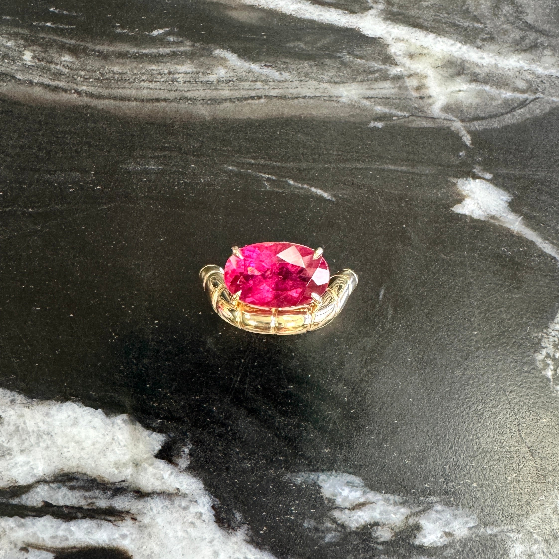 Gold ring with a curved band and an oval pink rubellite against a black and white marble background 