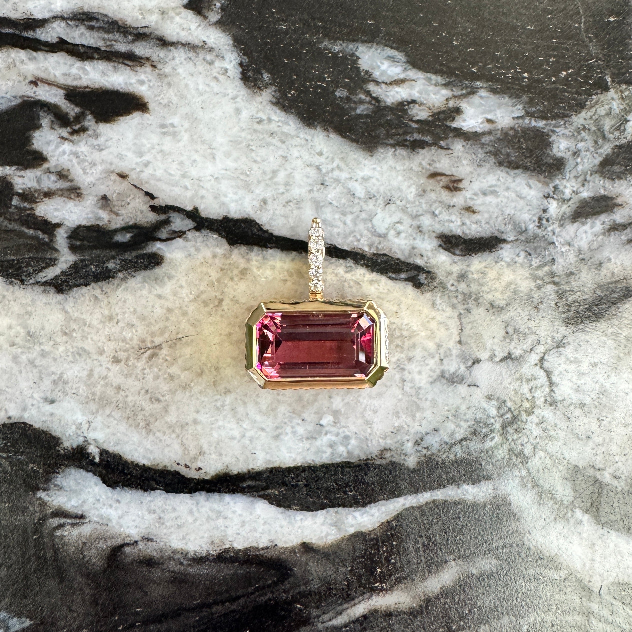 Gold pendant with emerald-cut pink tourmaline and a diamond bail against a black and white marble background