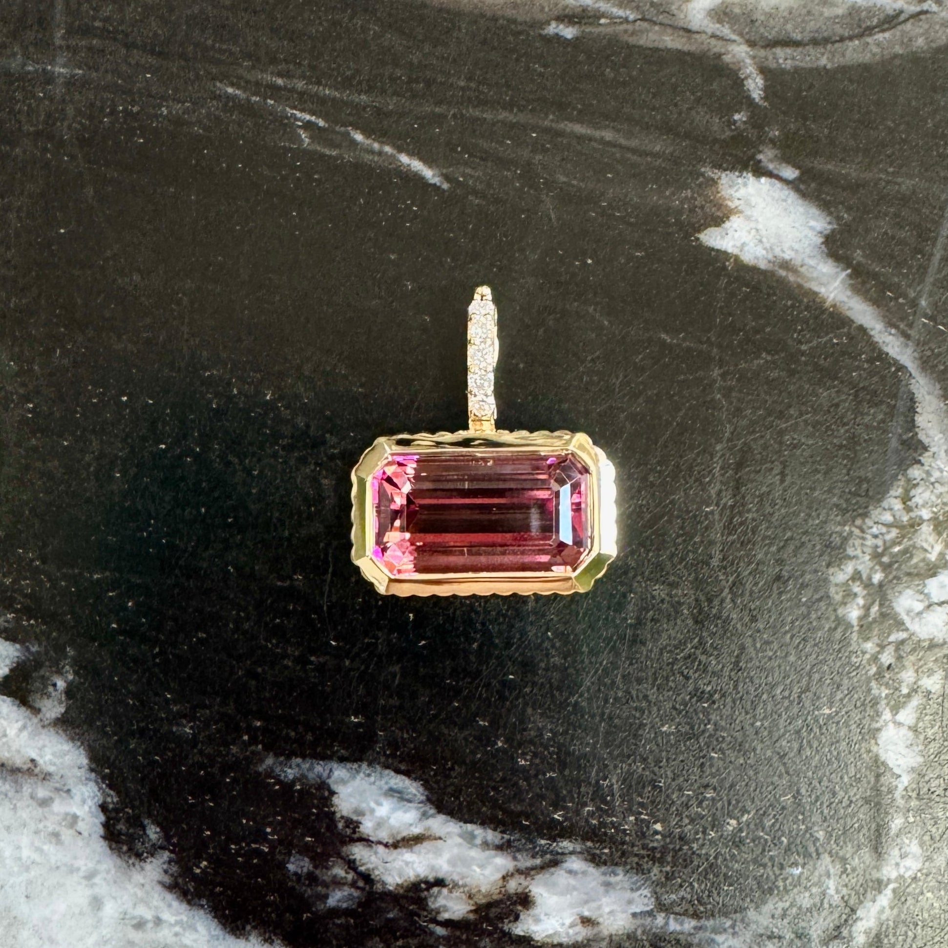 Gold pendant with emerald-cut pink tourmaline and a diamond bail against a black and white marble background