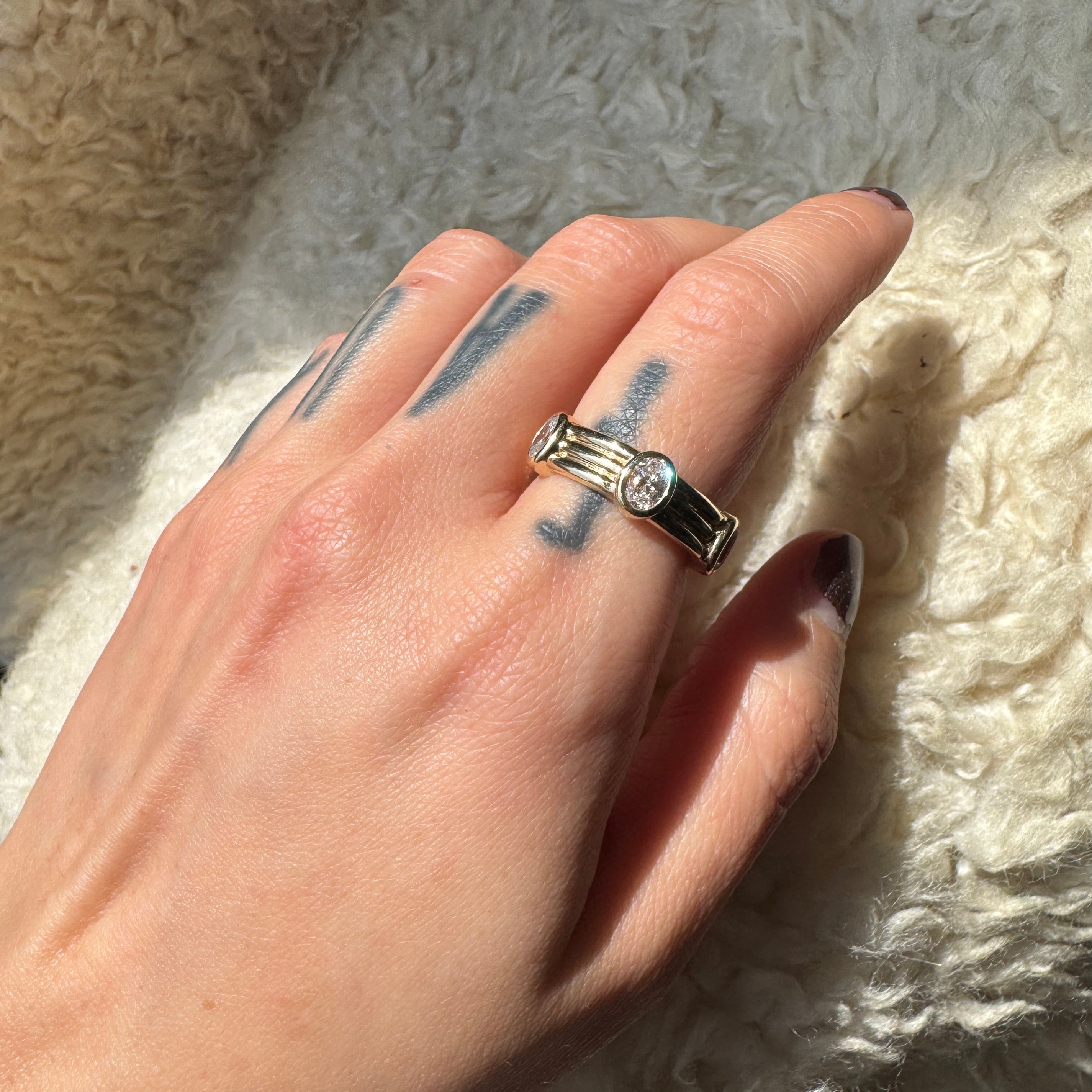 Hand wearing a ring with oval diamonds on a textured white surface