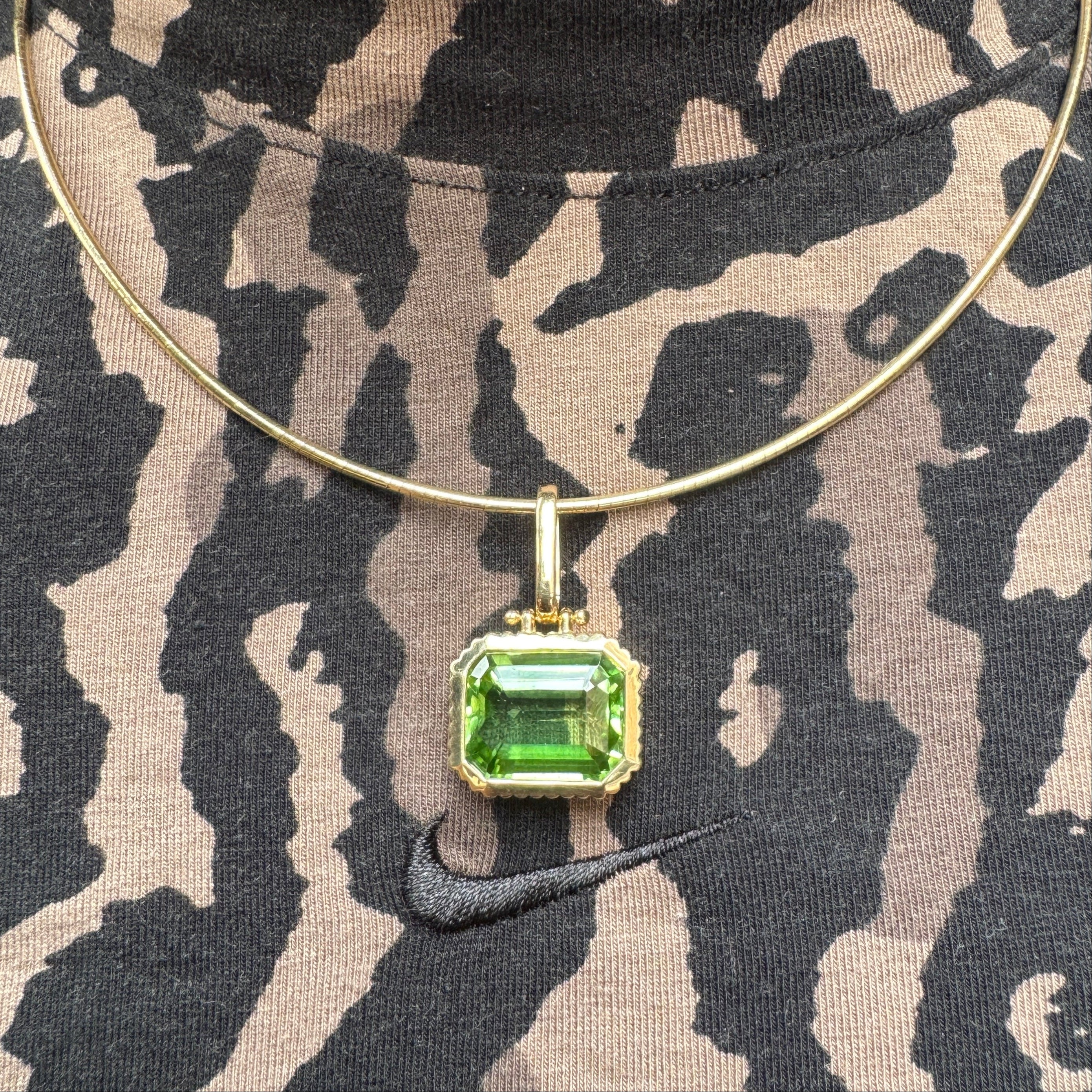 Gold necklace with a green gemstone pendant on a camouflage-patterned fabric background