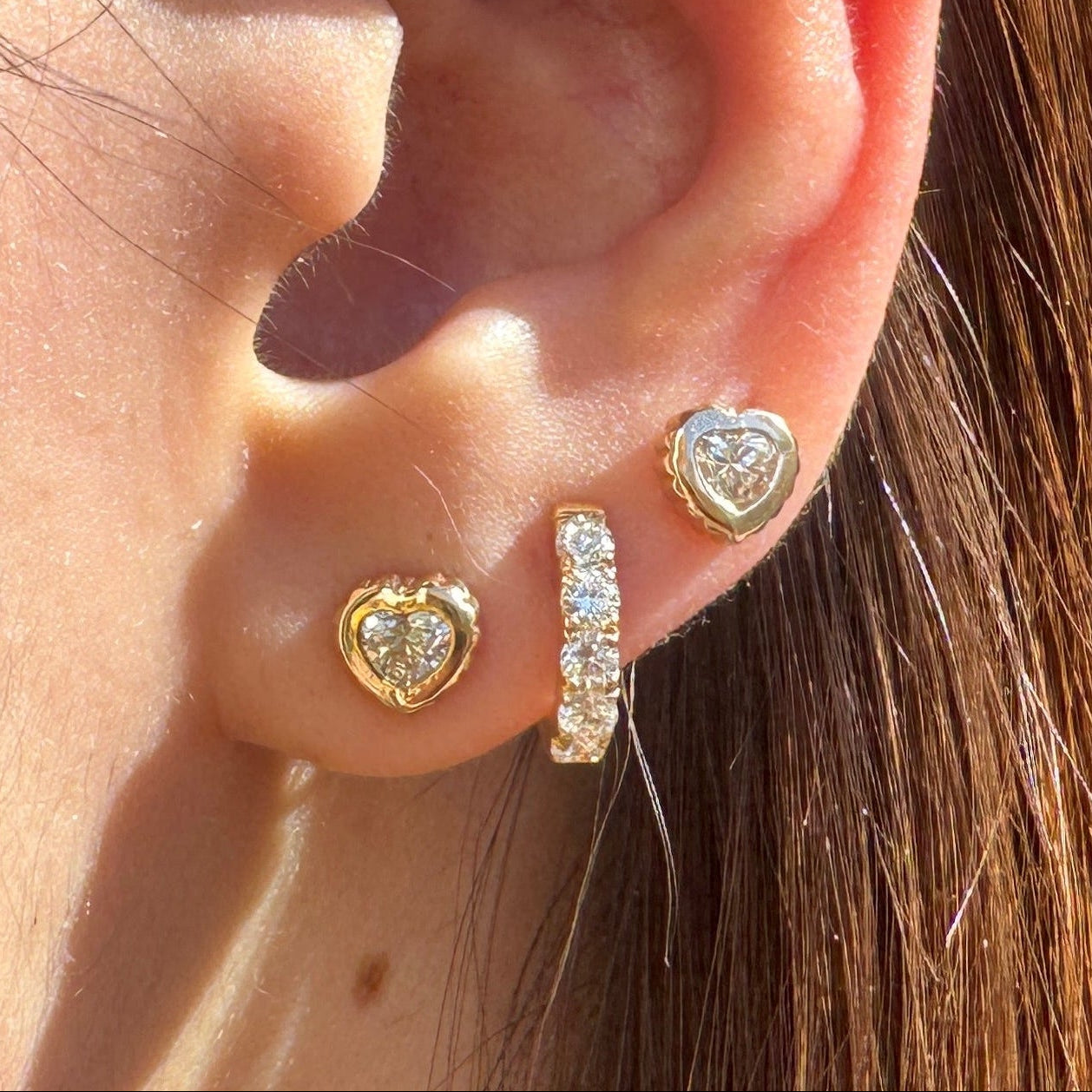 Close-up of an ear with multiple gold and diamond earrings, including two gold earrings with heart-shaped diamonds