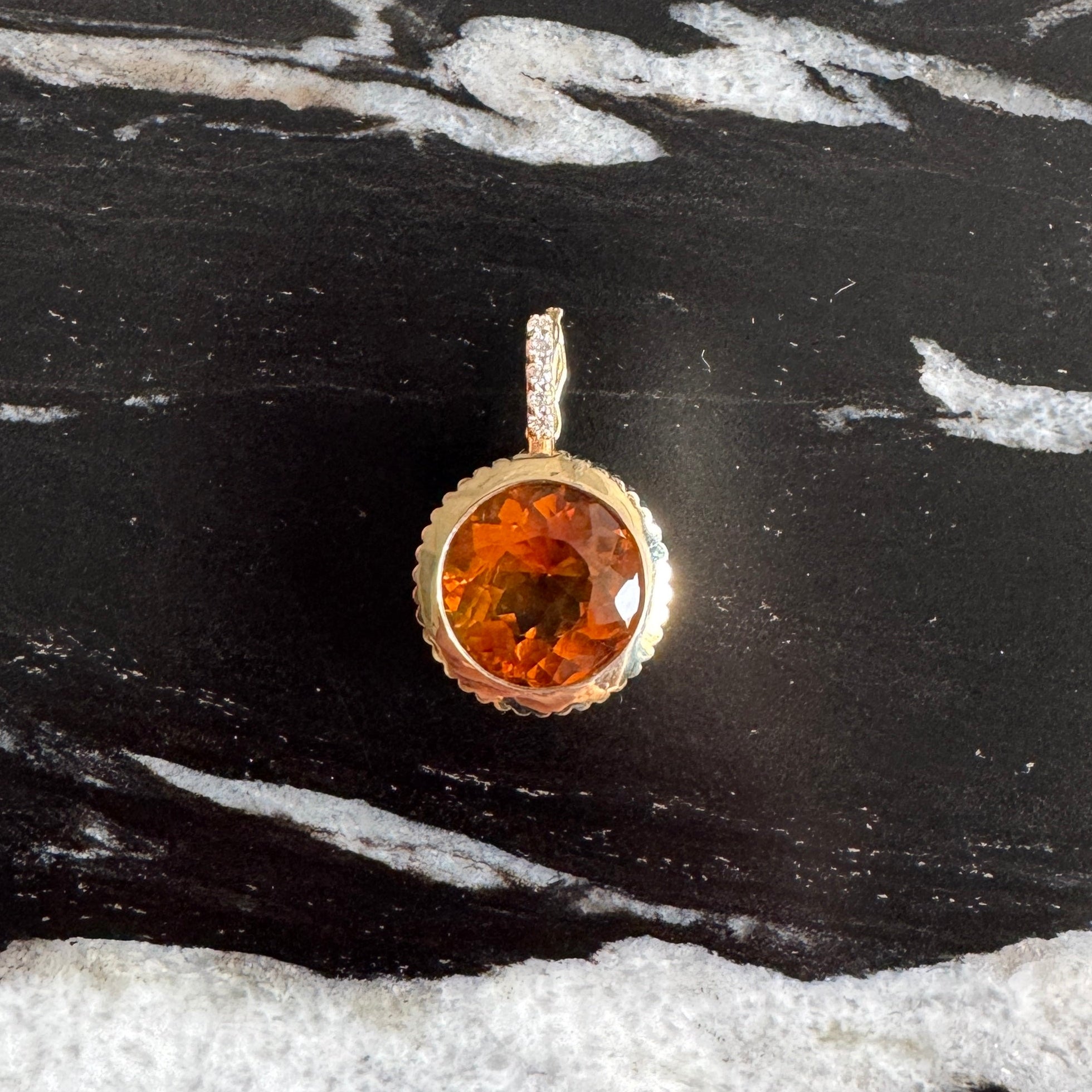 Gold pendant with an orange citrine against black and white marble background