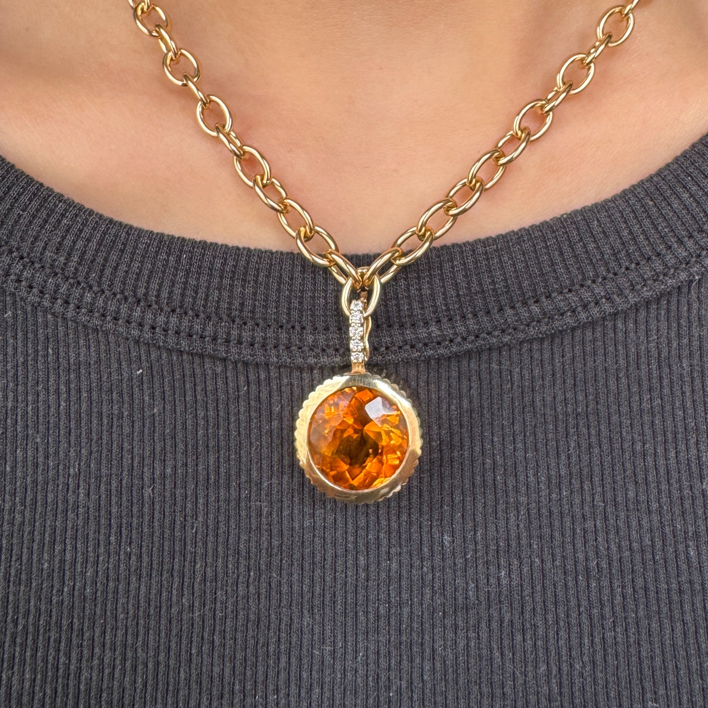 Person wearing a round gold pendant with an orange citrine on a gold chain against a black shirt