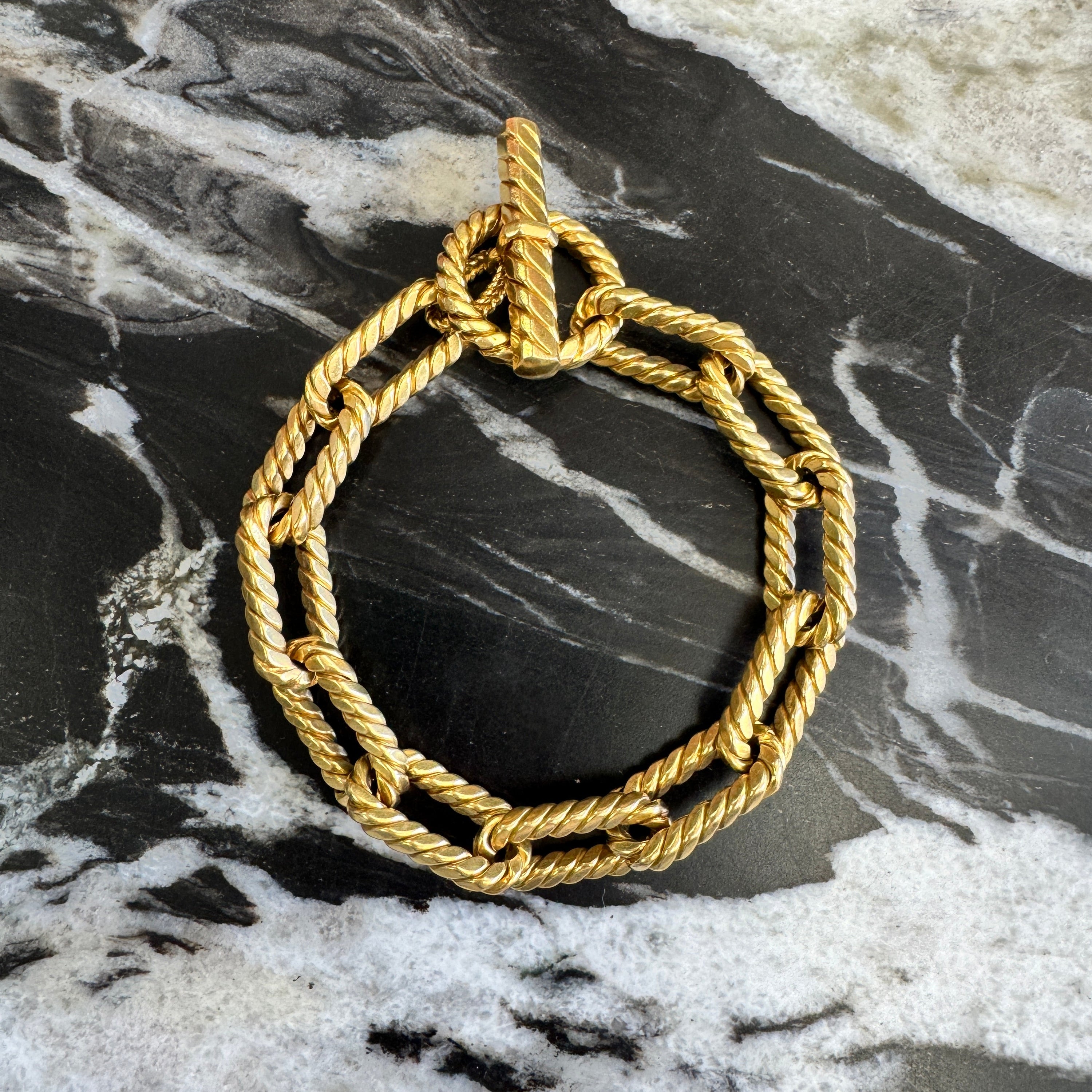 Gold rope-style brooch on a marble surface