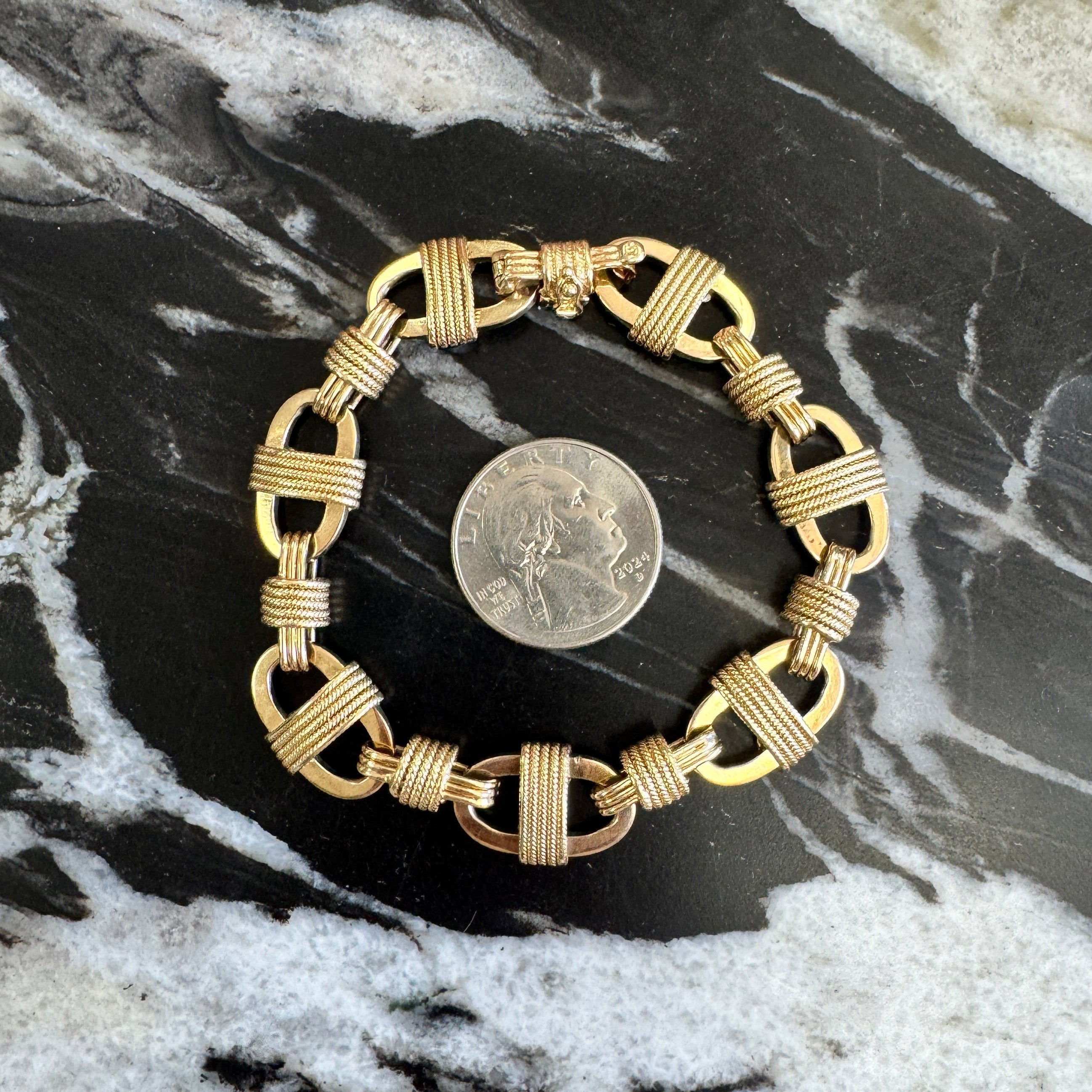 Gold bracelet on a marble surface with a coin for scale