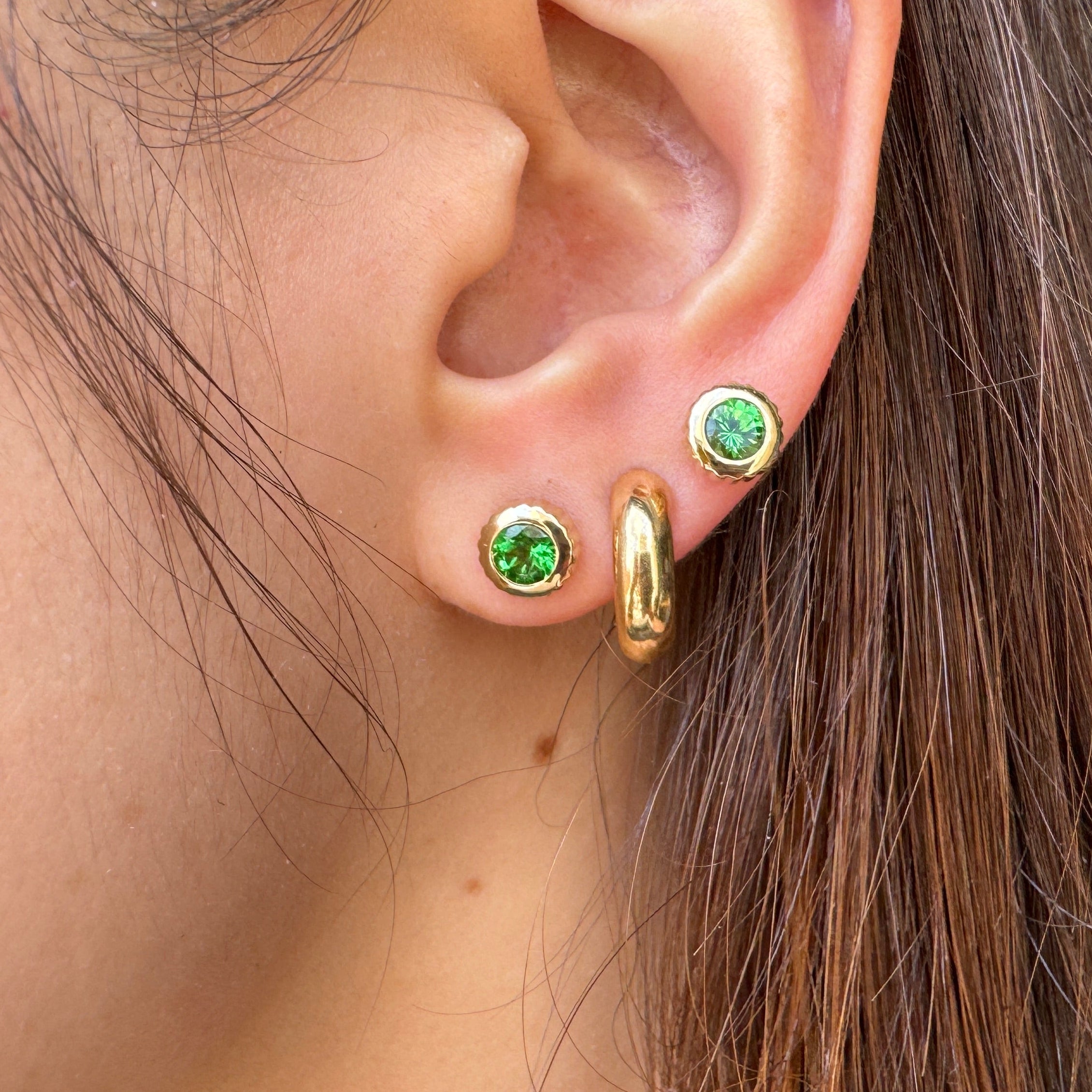 Close-up of an ear wearing gold earrings including two round gold studs with green tsavorites