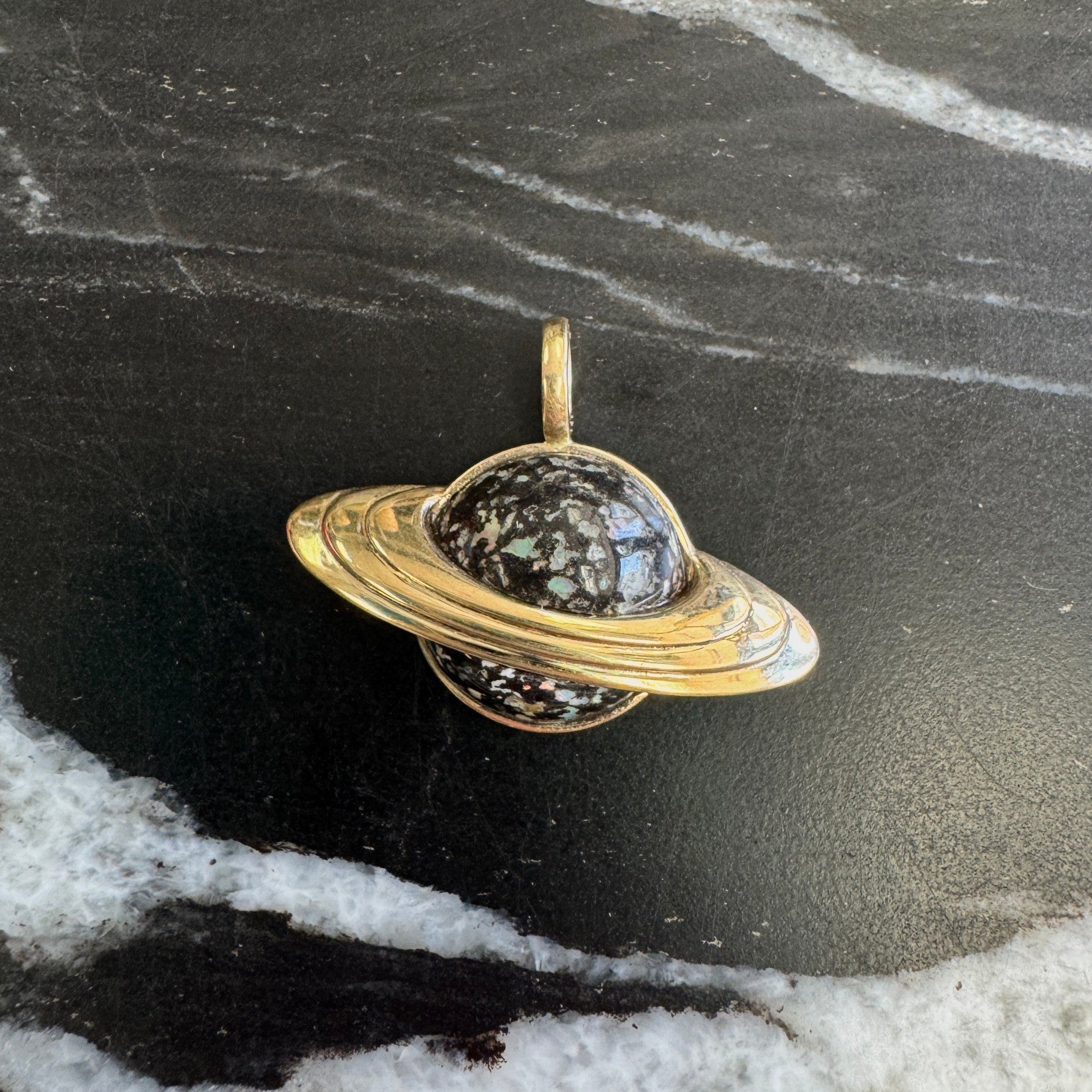 Gold Saturn pendant on a dark marble surface