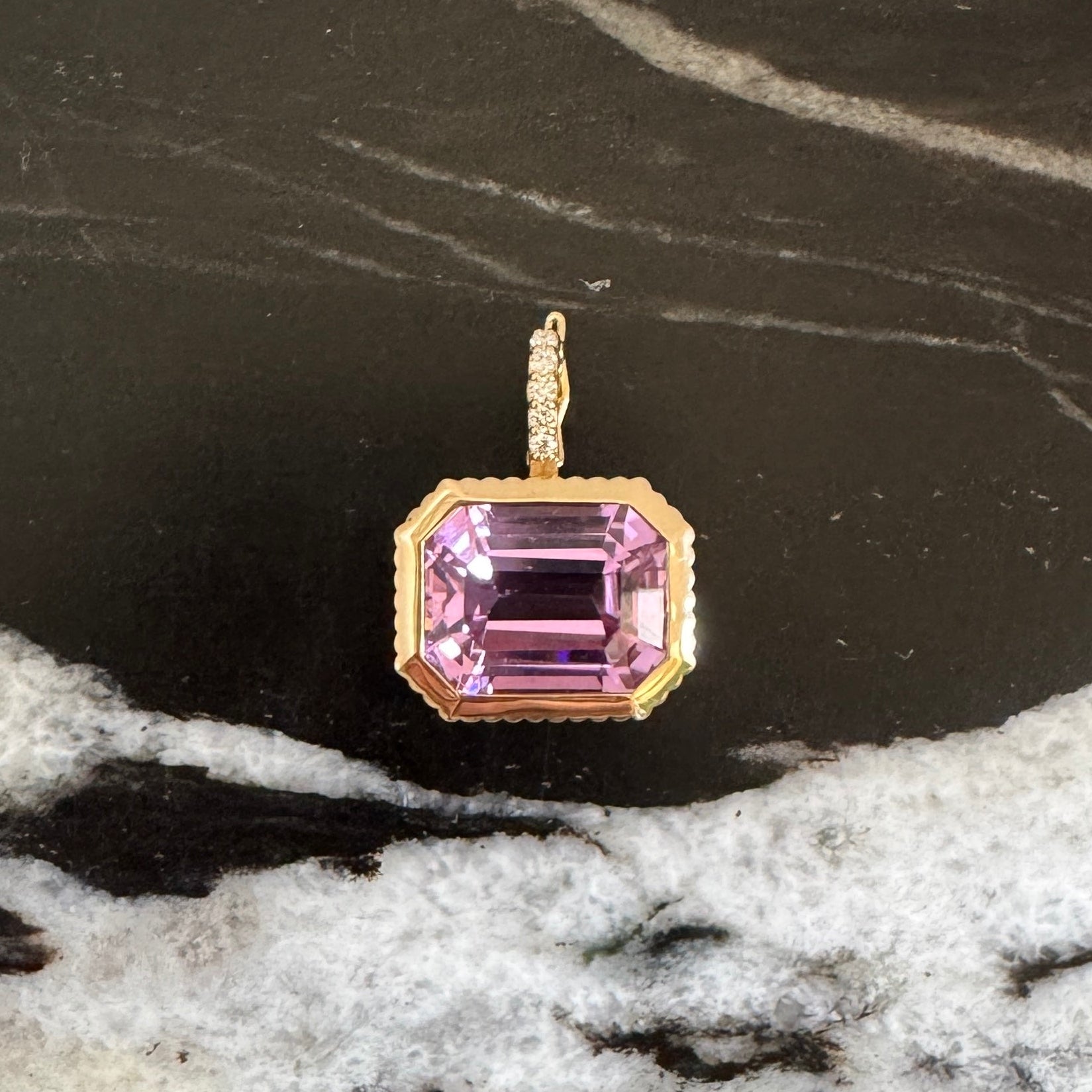 Gold pendant with a purple kunzite  and a diamond bail against a black and white  marble background 