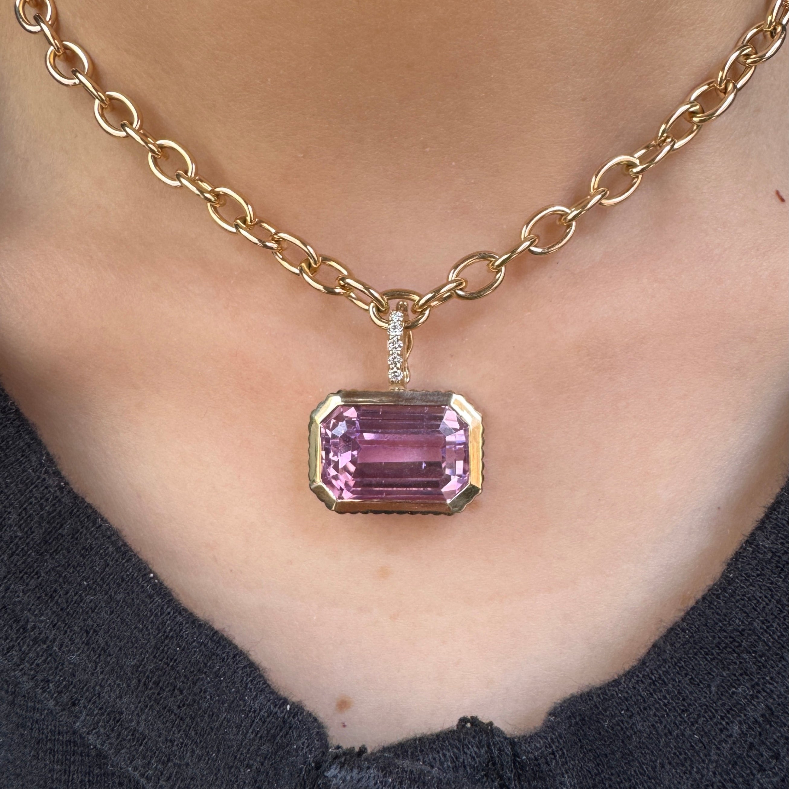 Person wearing a Gold pendant with a purple kunzite  and a diamond bail on a gold chain 