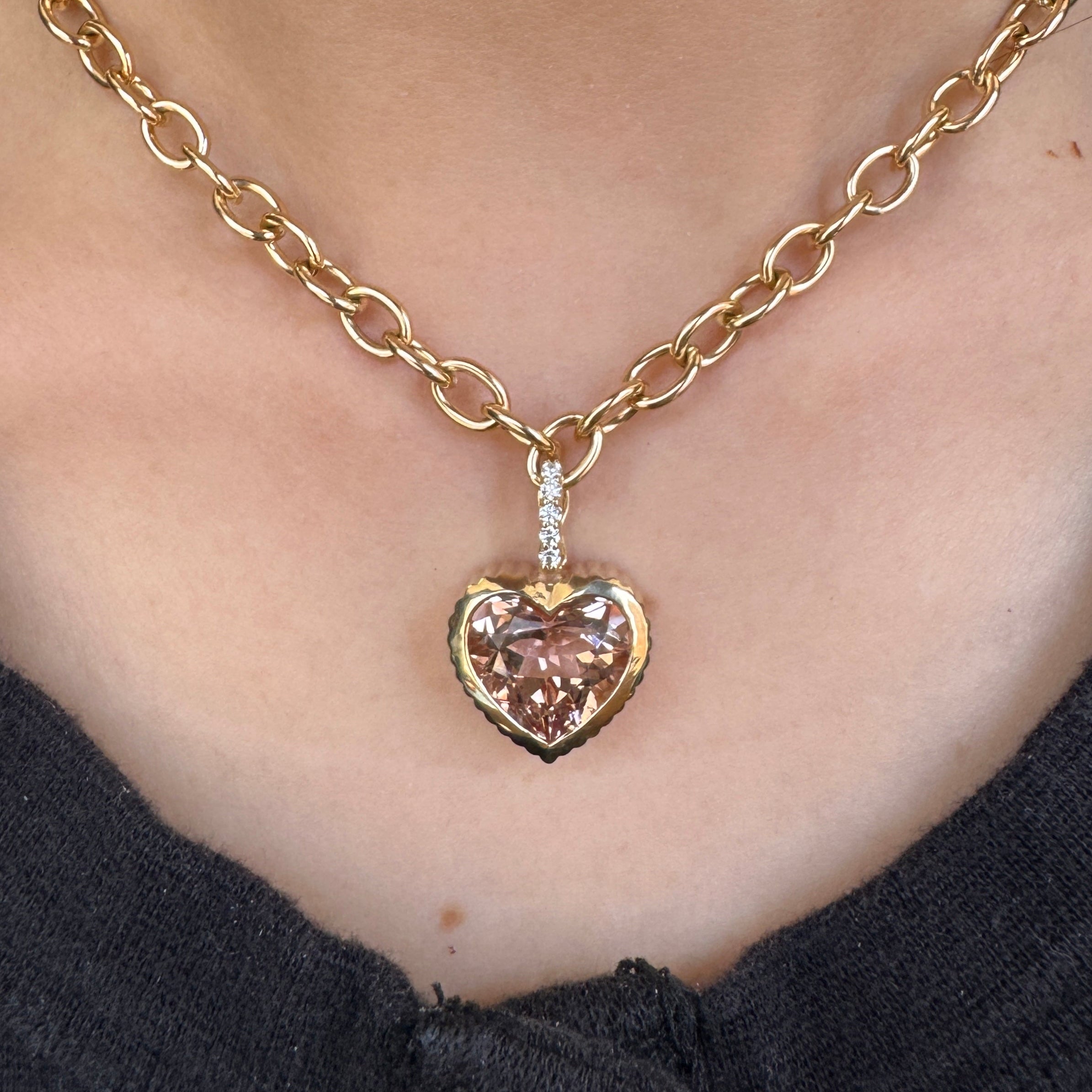 Person wearing a heart-shaped gold pendant with a peachy morganite  and a diamond bail on a gold chain 