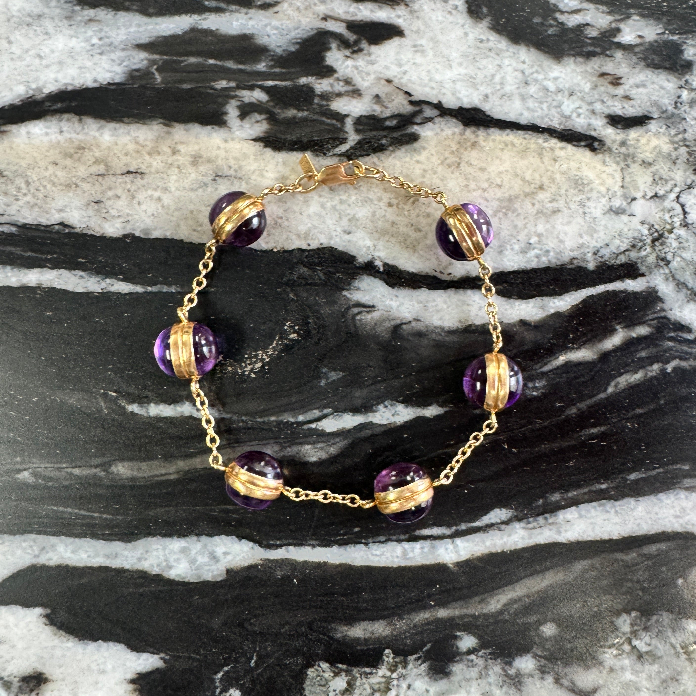 Gold bracelet with purple beads on a marble surface