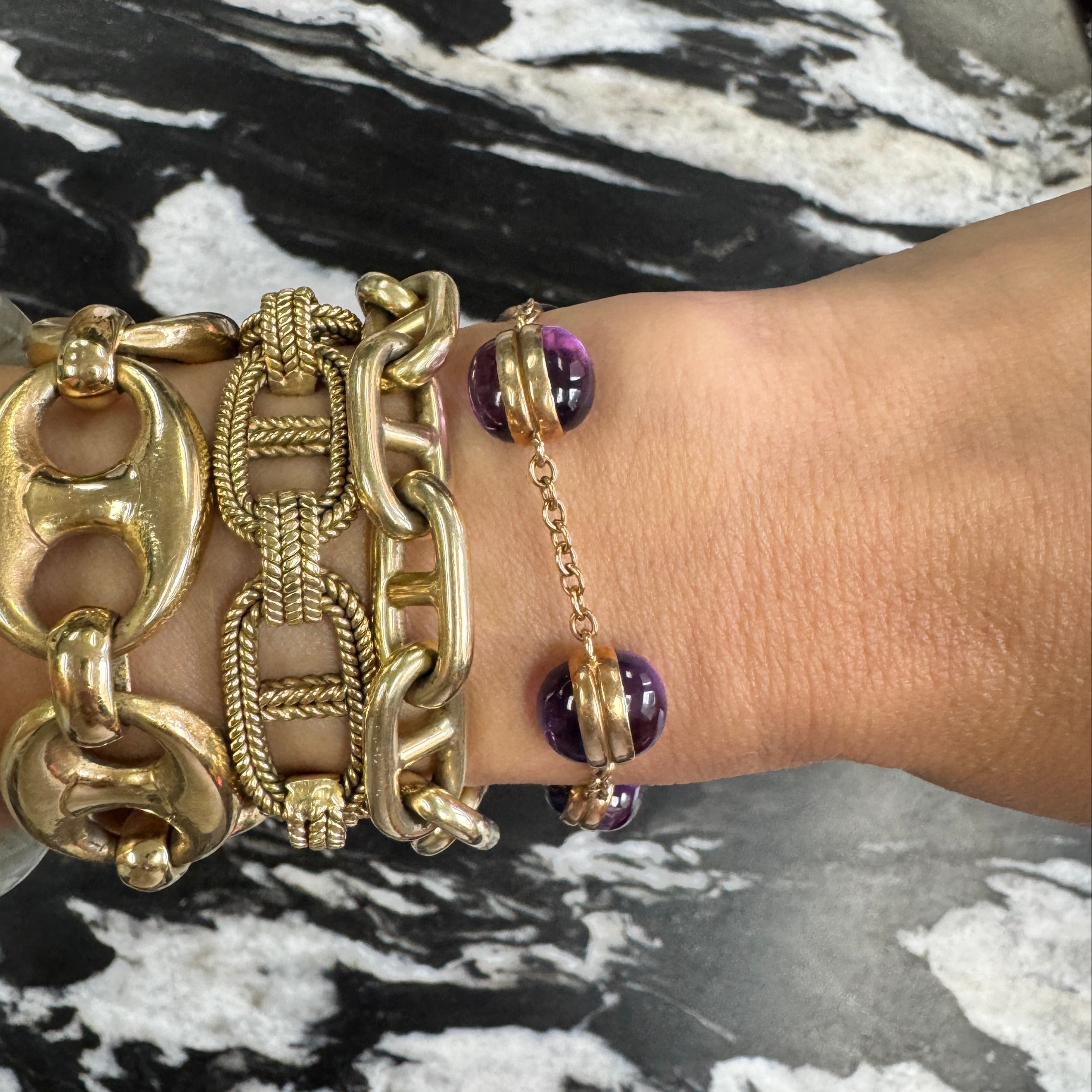 Gold chain bracelet with purple beads on a marble surface