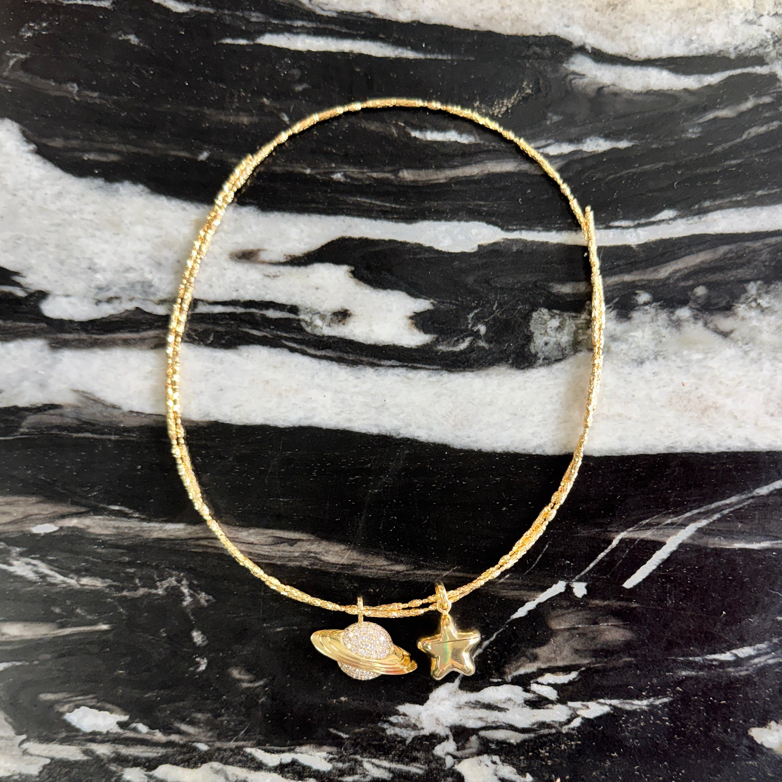 Gold necklace with star and leaf charms on a black and white marble surface