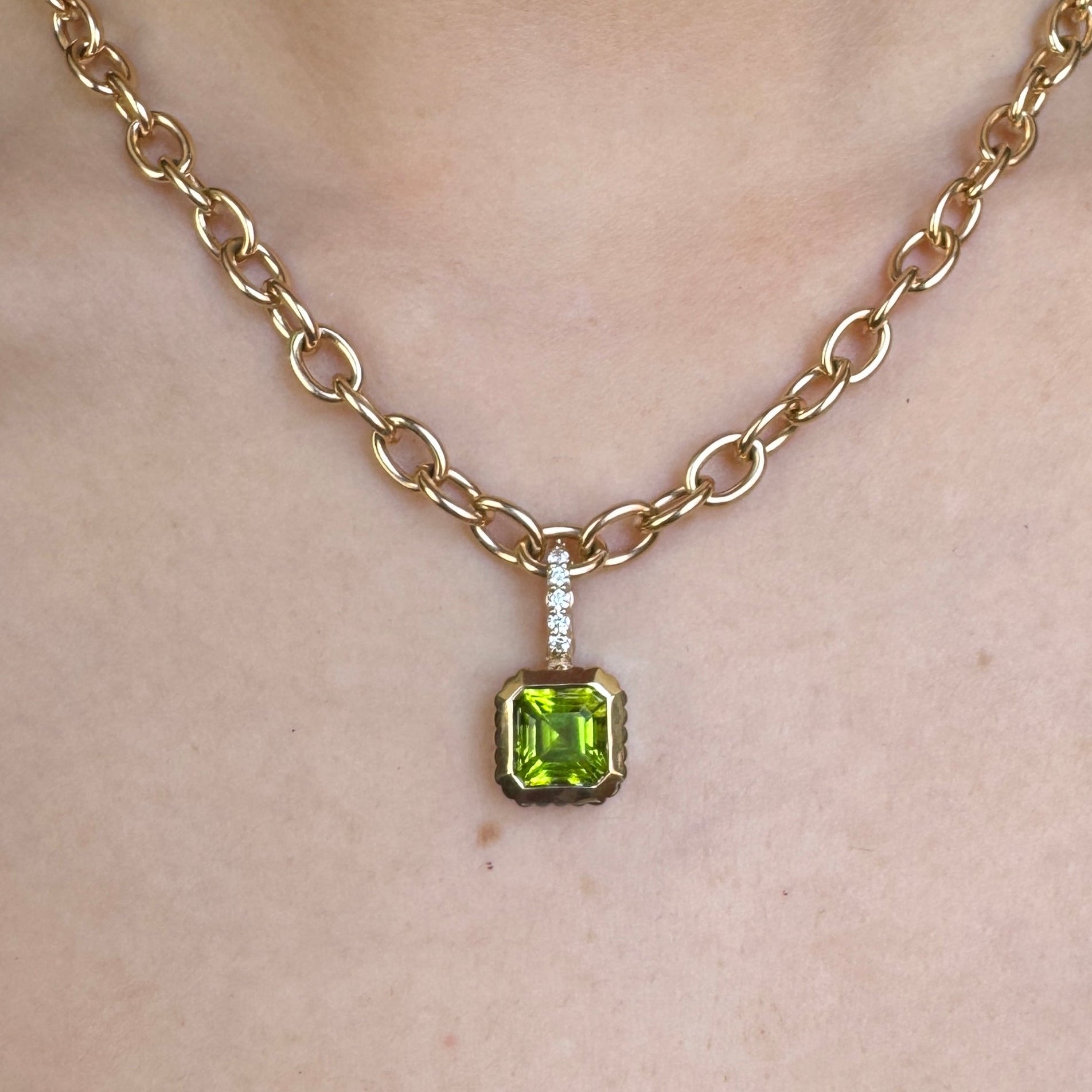 Person wearing a Gold pendant with a square-cut green peridot and a diamond bail on a gold chain
