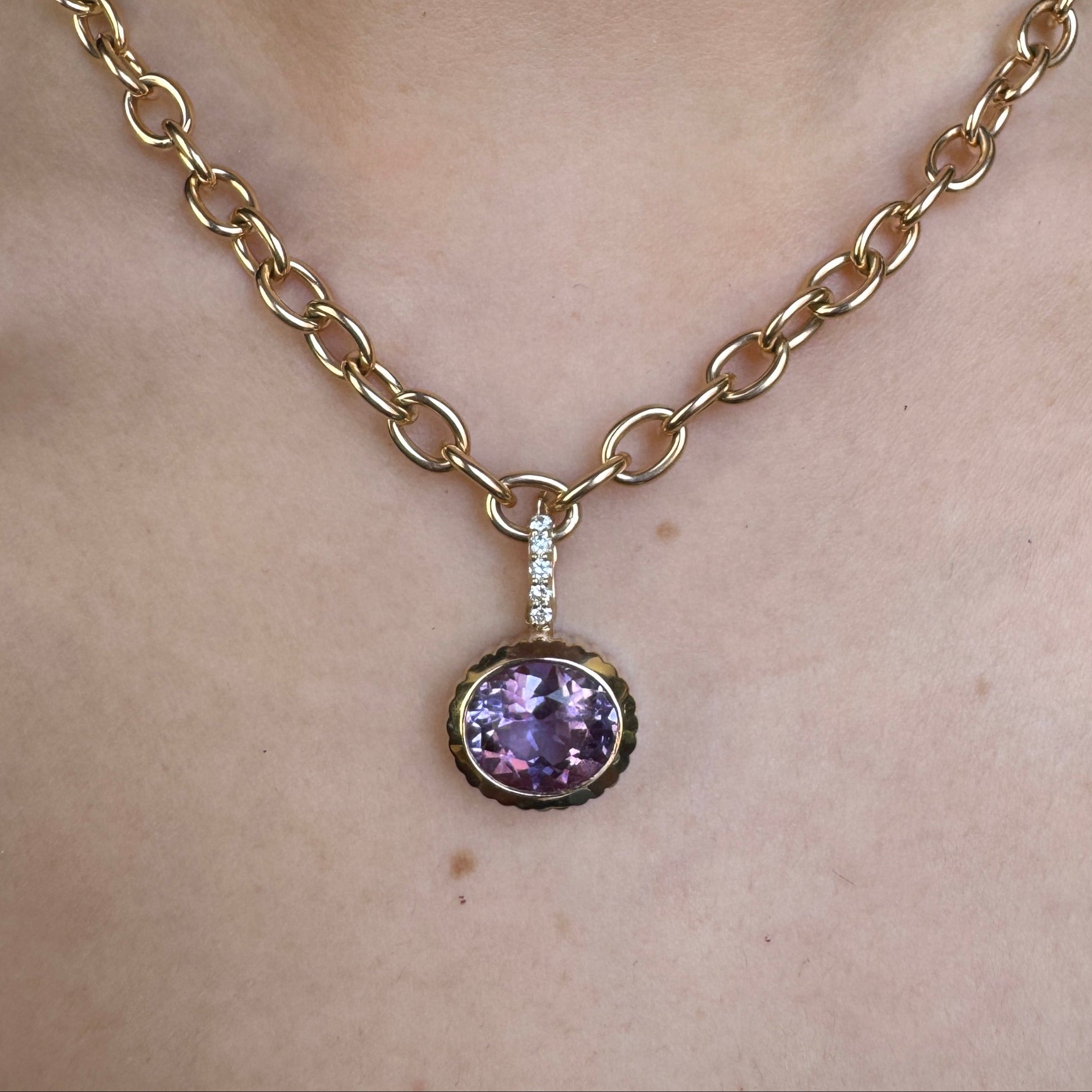 Person wearing a gold pendant with an oval-cut purple amethyst and a diamond bail on a gold chain