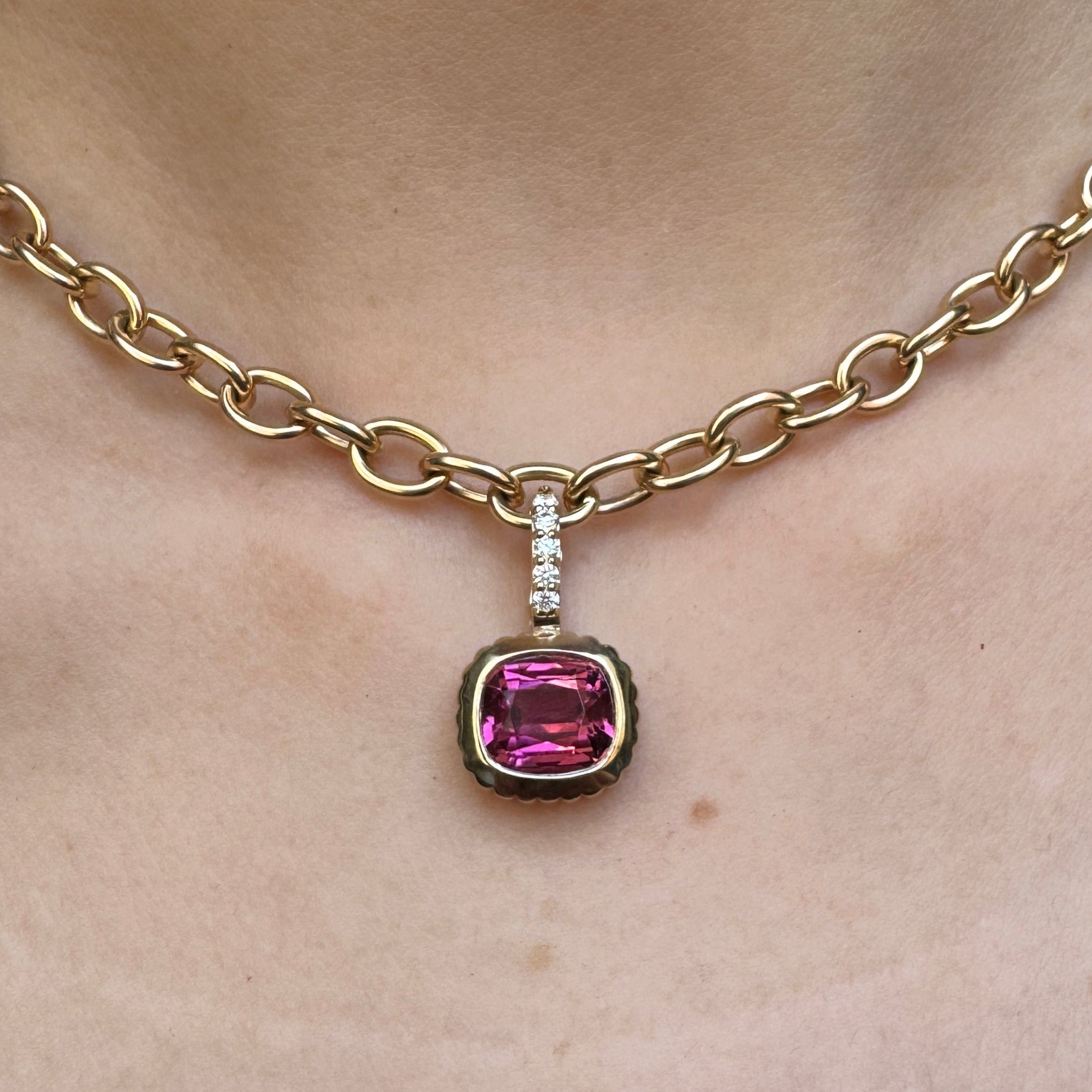 Person wearing a gold pendant with a cushion-cut pink tourmaline and a diamond bail on a gold chain