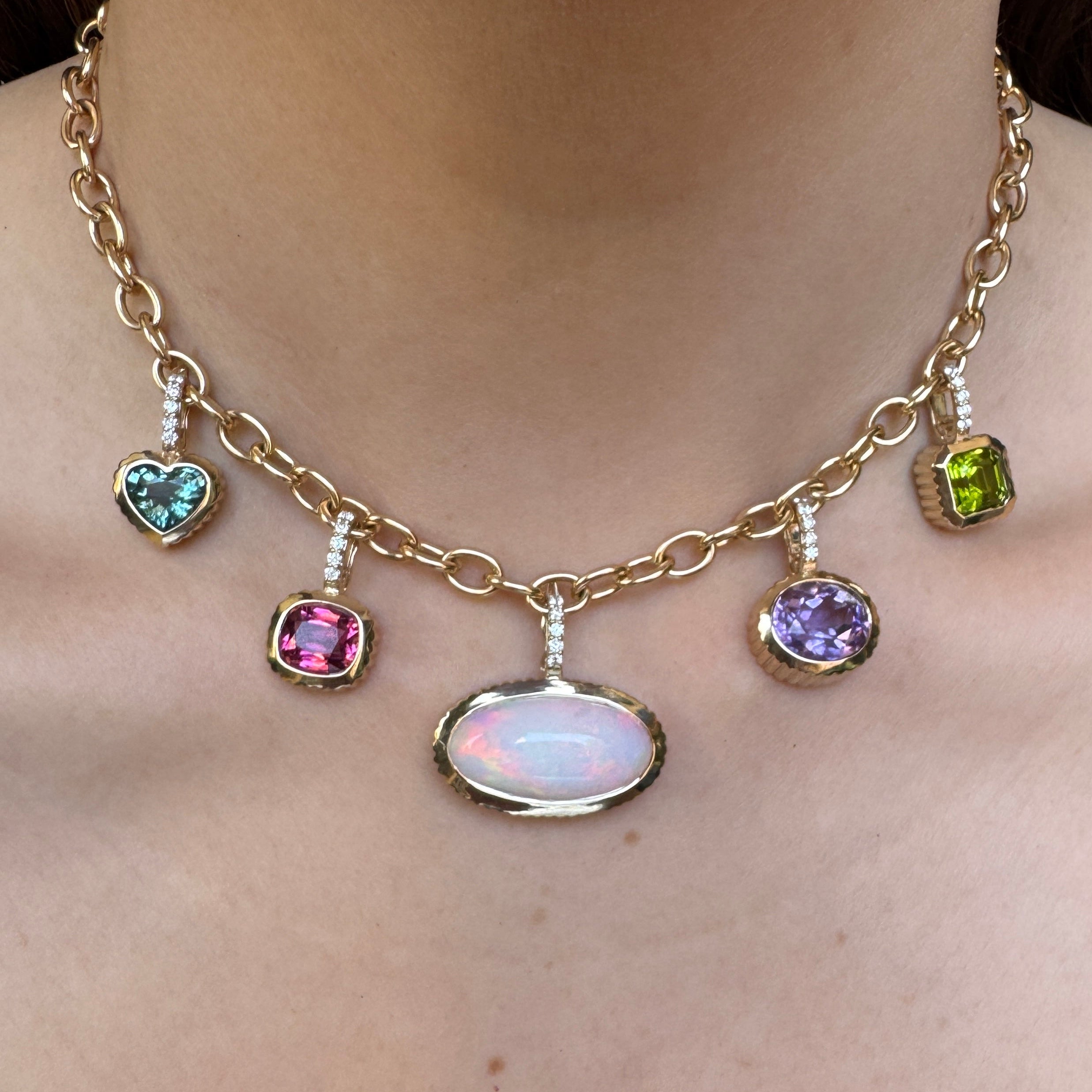 Person wearing a gold chain with multiple gold and multicolored gemstone pendants 