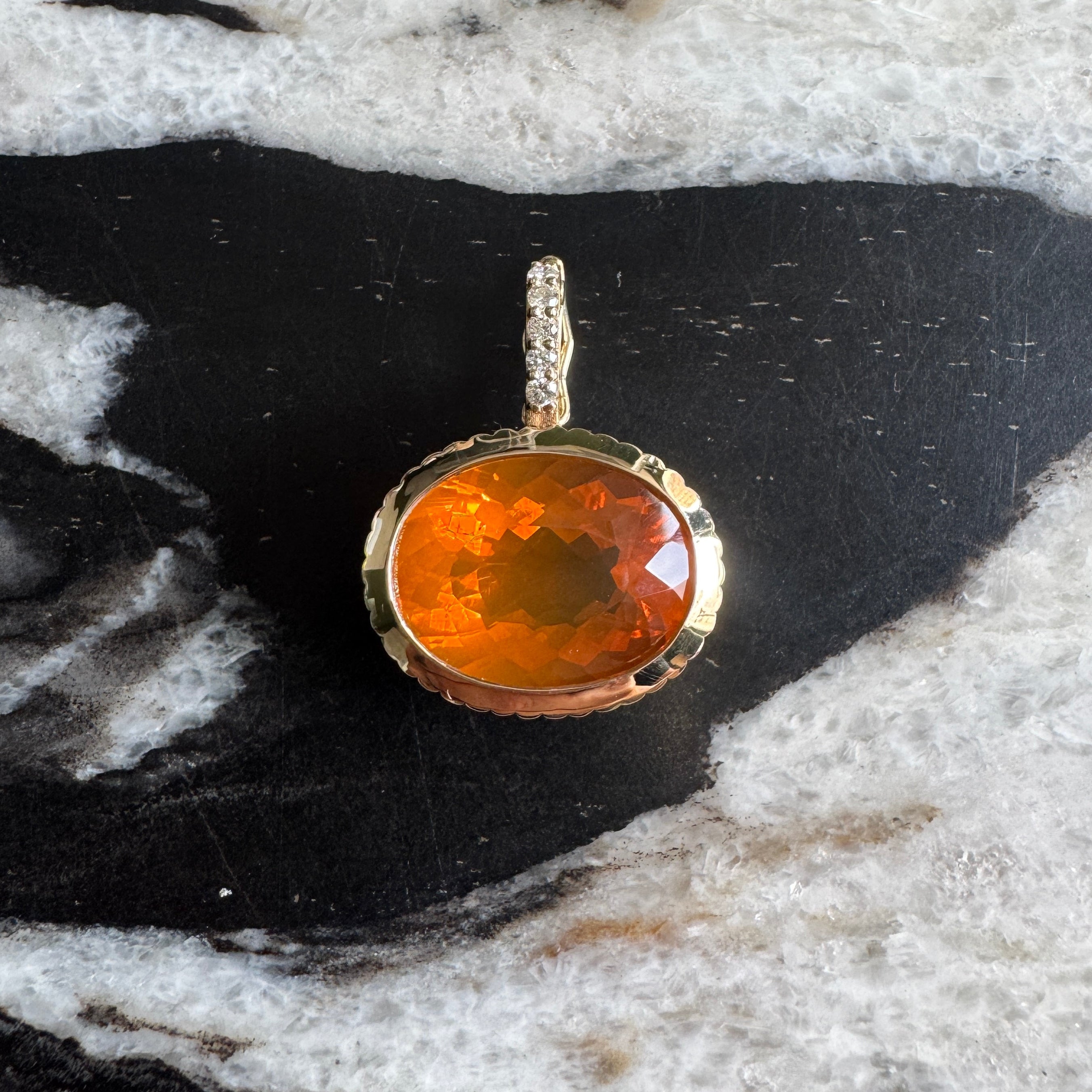 Gold pendant with an oval-cut fire opal and diamond bail against a black and white marble background