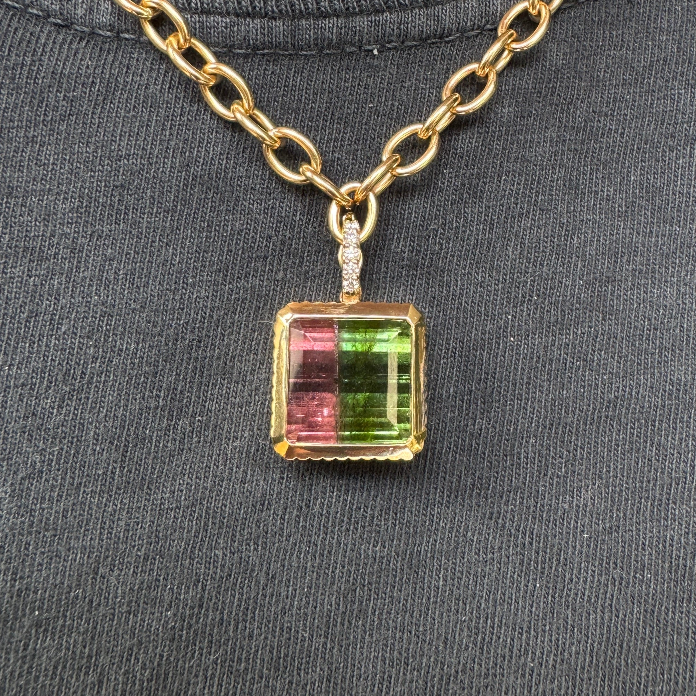 Person wearing a gold pendant with an emerald-cut watermelon tourmaline and a diamond bail on a gold chain against a black top