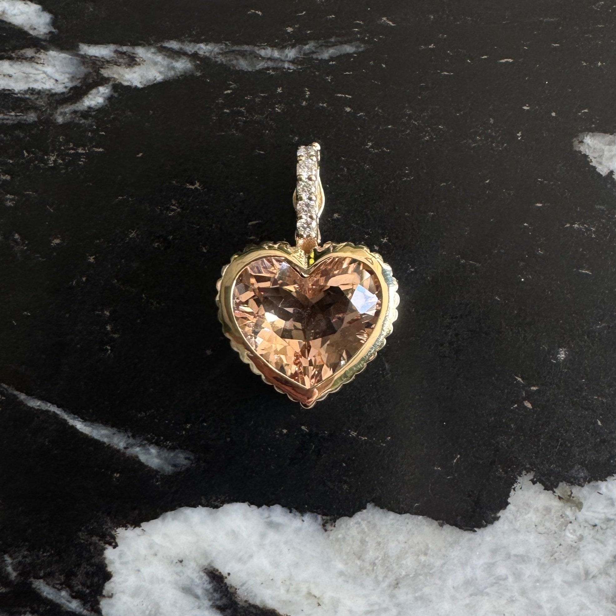 Gold Pendant with a peachy heart-shaped morganite and a diamond bail against a black and white marble background 