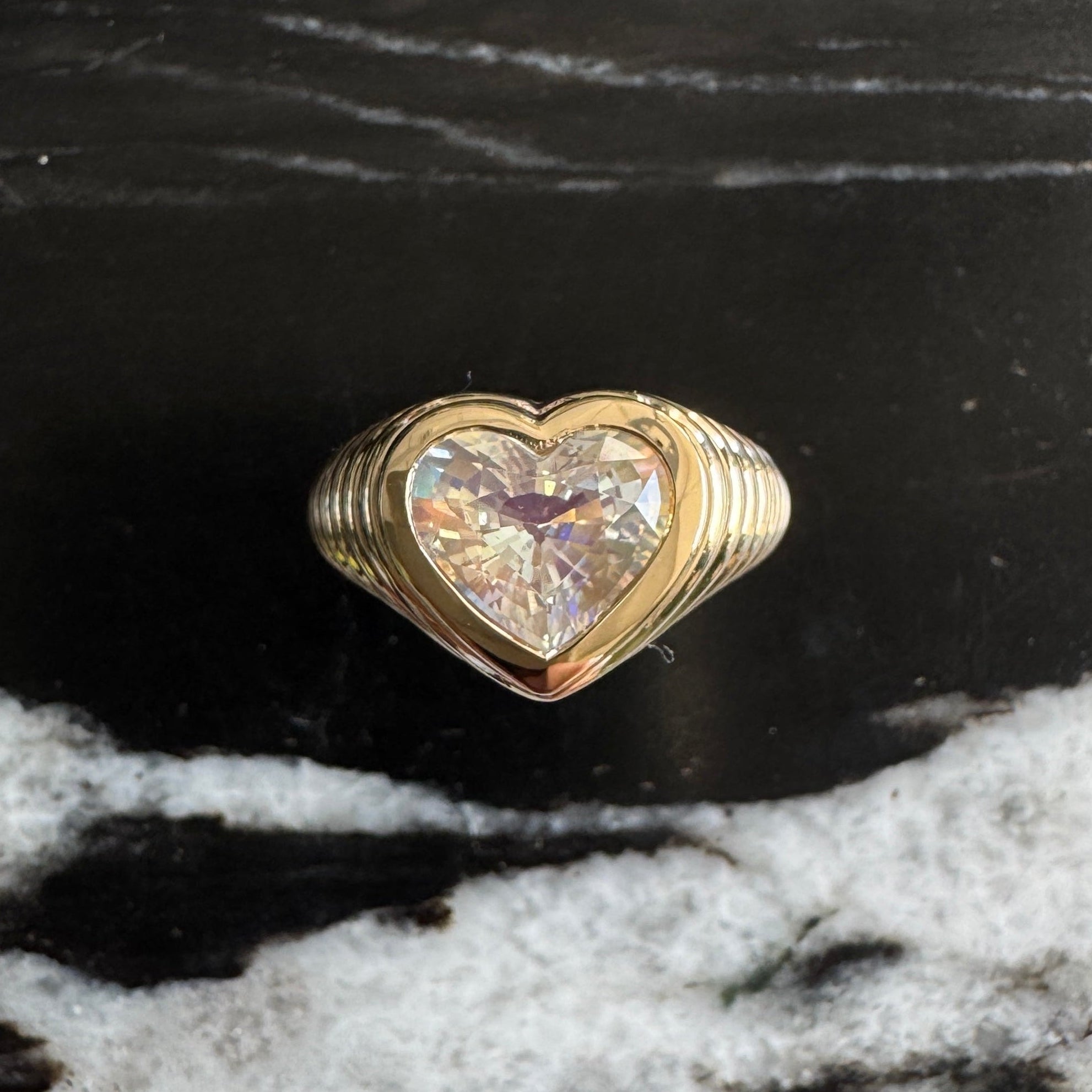 Gold ring with a heart-shaped rainbow moonstone against a black and white marble background 