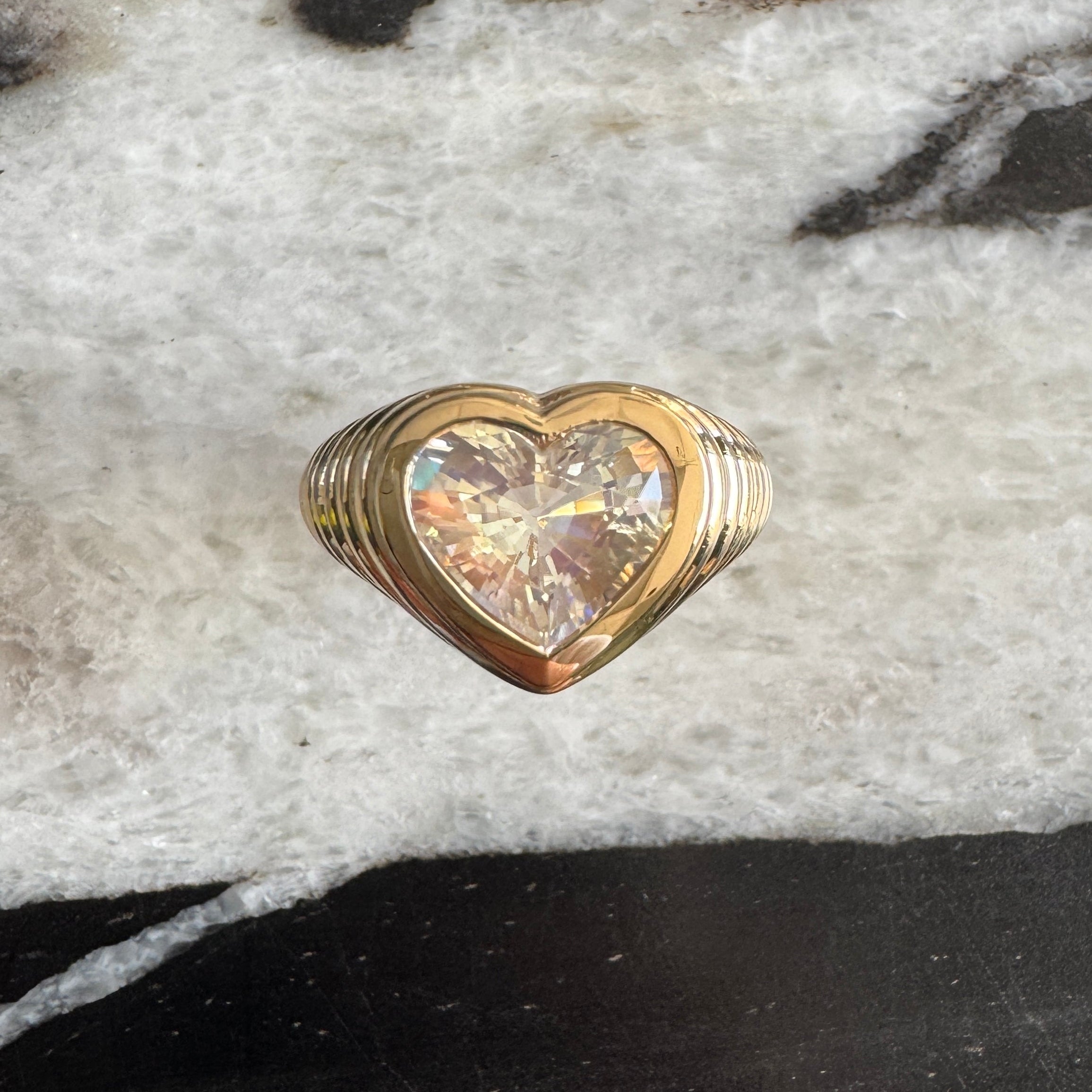 Gold ring with a heart-shaped rainbow moonstone against a black and white marble background 