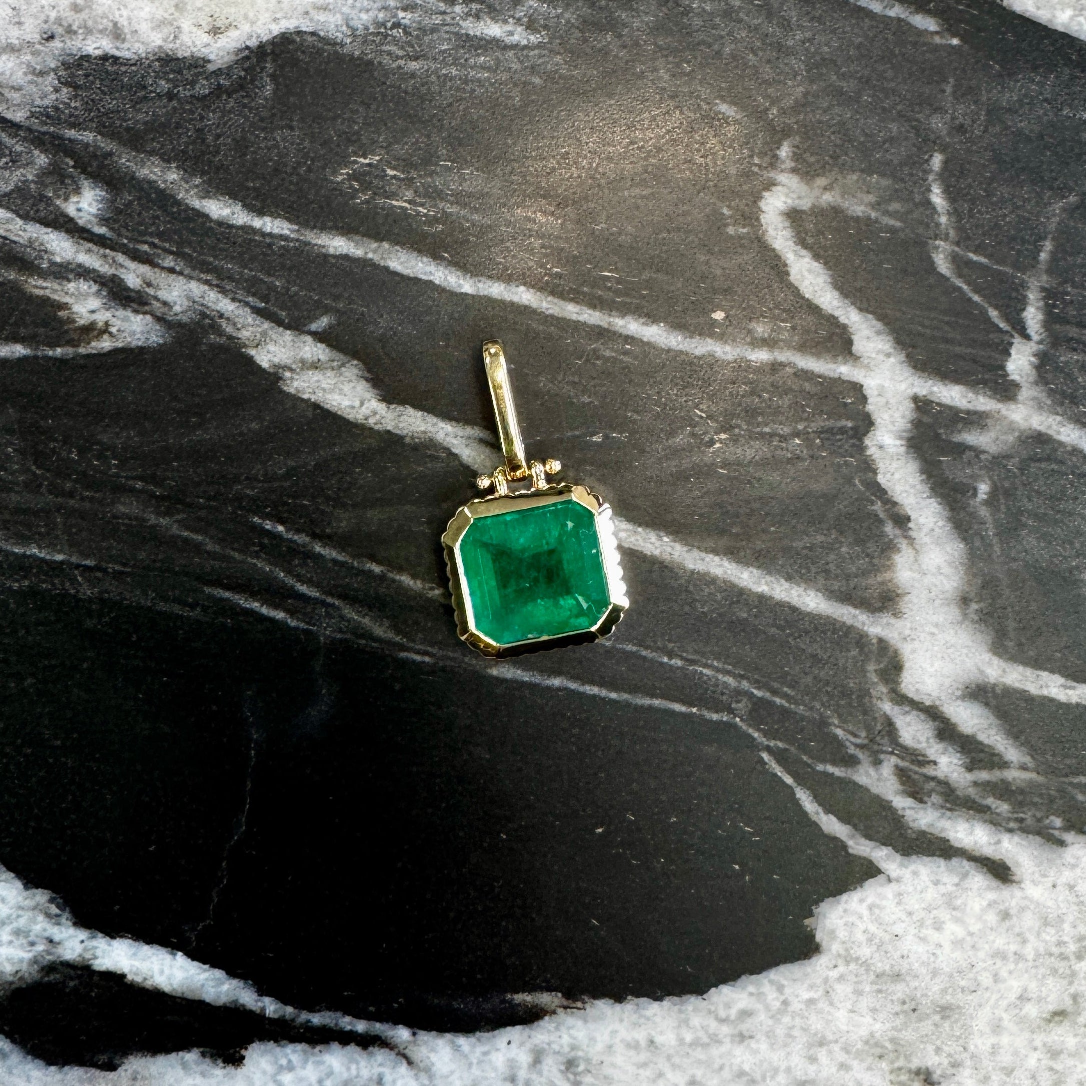 Gold pendant with a emerald gemstone on a marble surface
