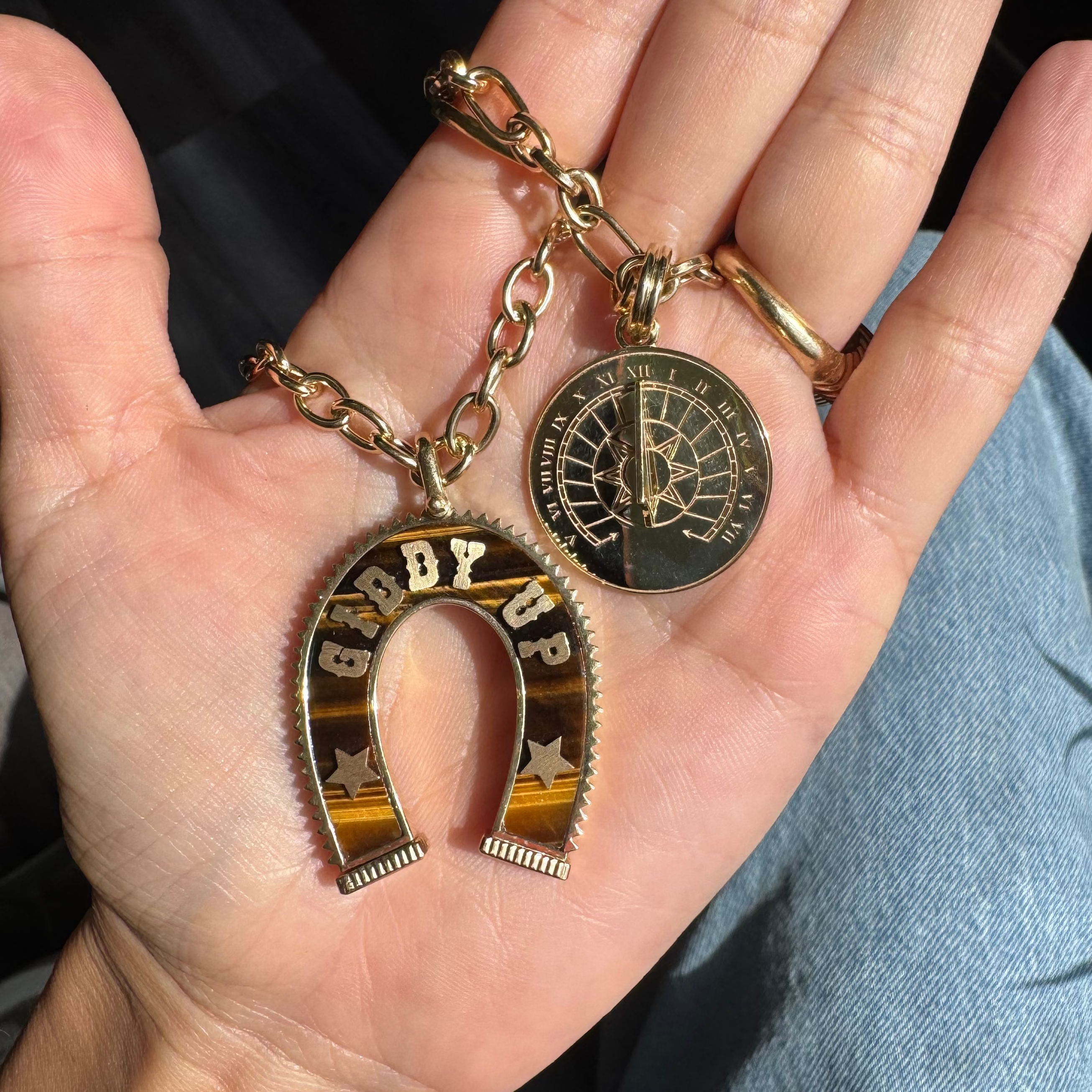 A gold-tone horseshoe-shaped keychain with 'GIDDY UP' lettering and a compass keychain, held in a person's hand.