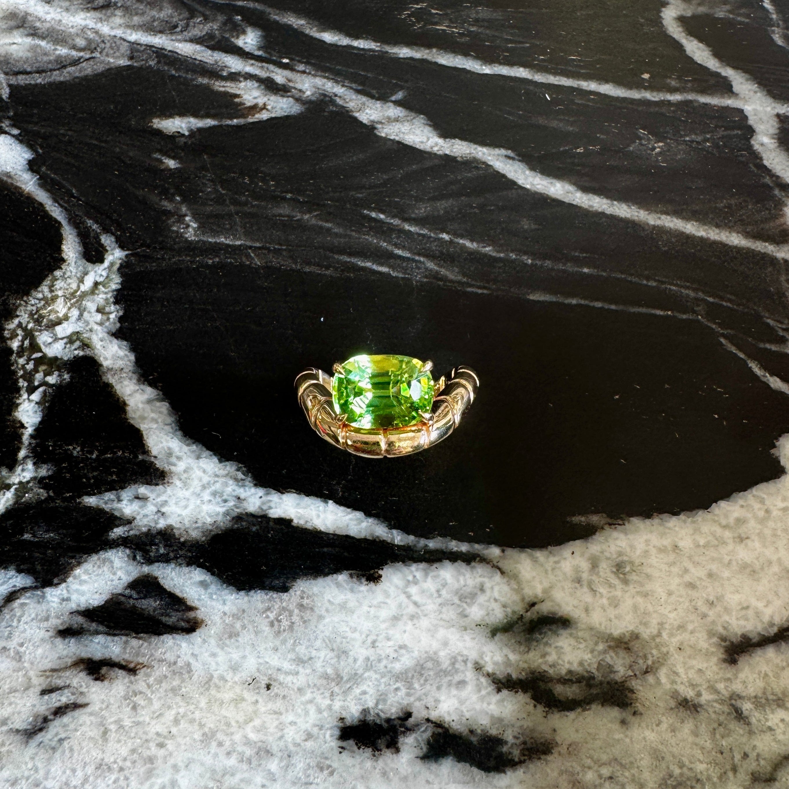 Gold ring with a green gemstone on a black and white marbled surface