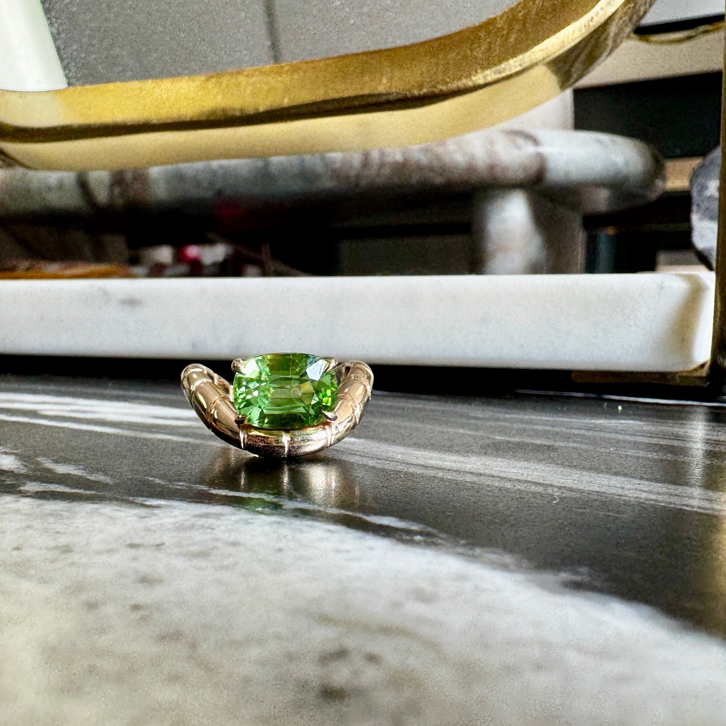 Small green gemstone on a marble surface with a gold-framed mirror in the background.