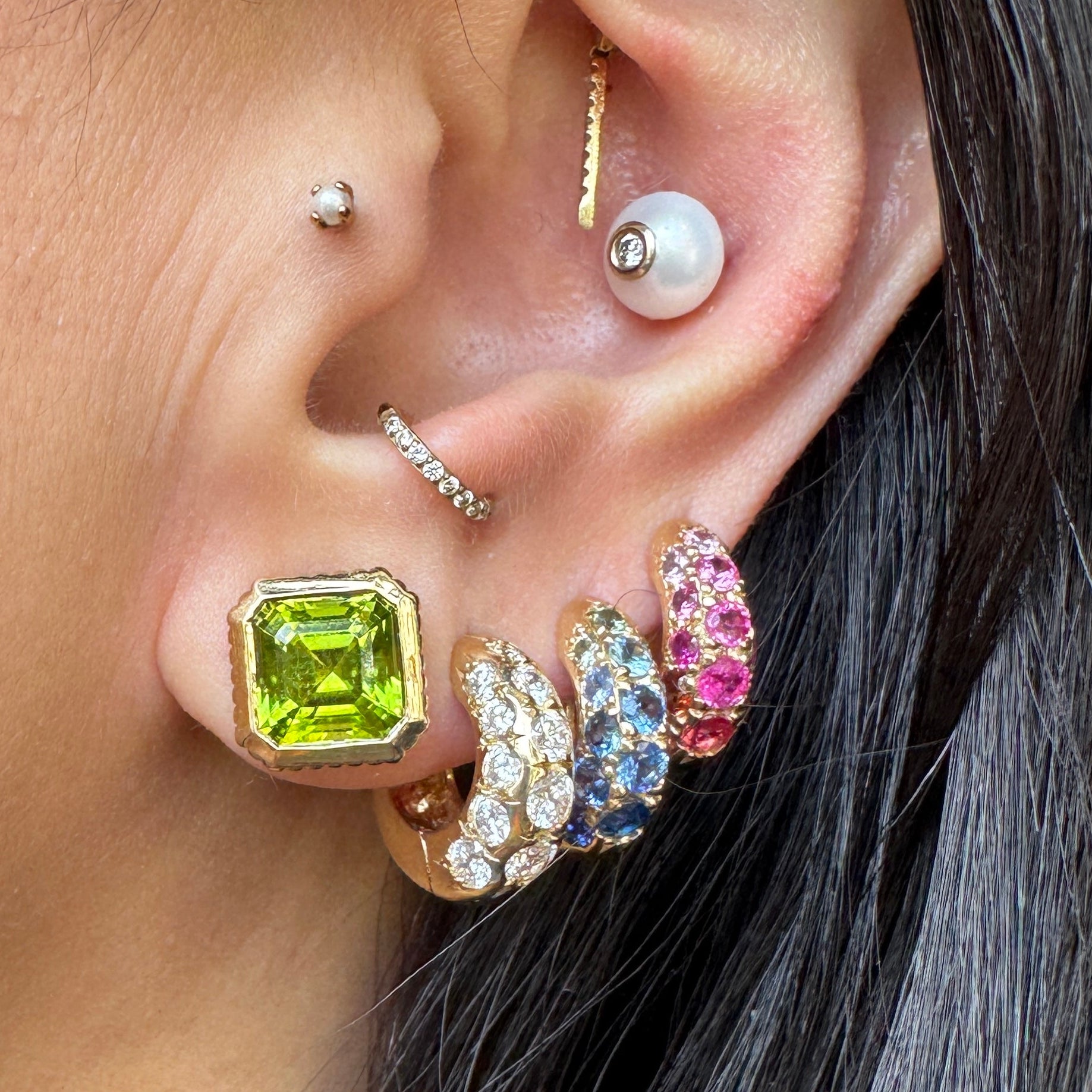 Close-up of an ear with multiple earrings including a green gemstone earring.