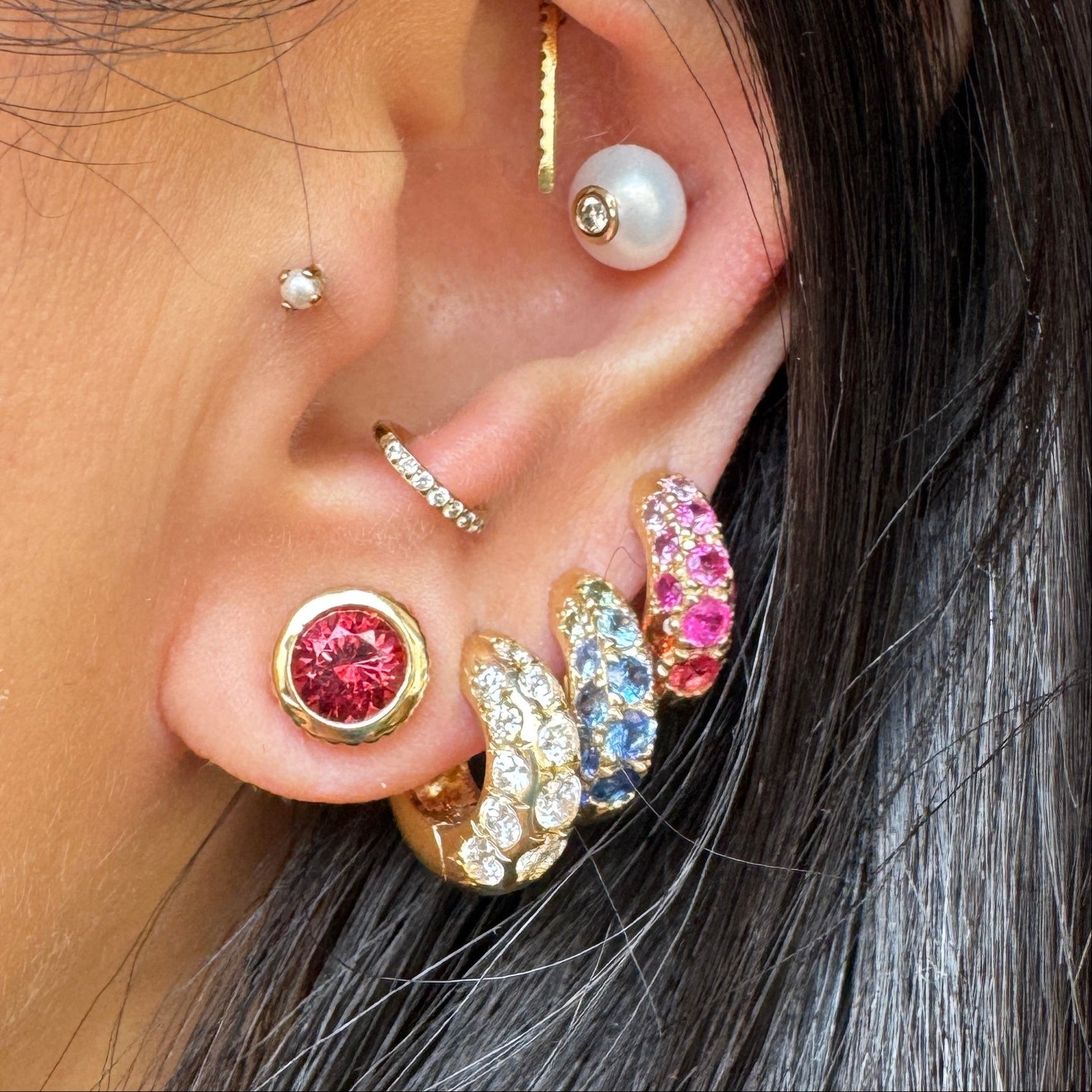 Close-up of an ear with multiple earrings and a pearl, with a blurred background.