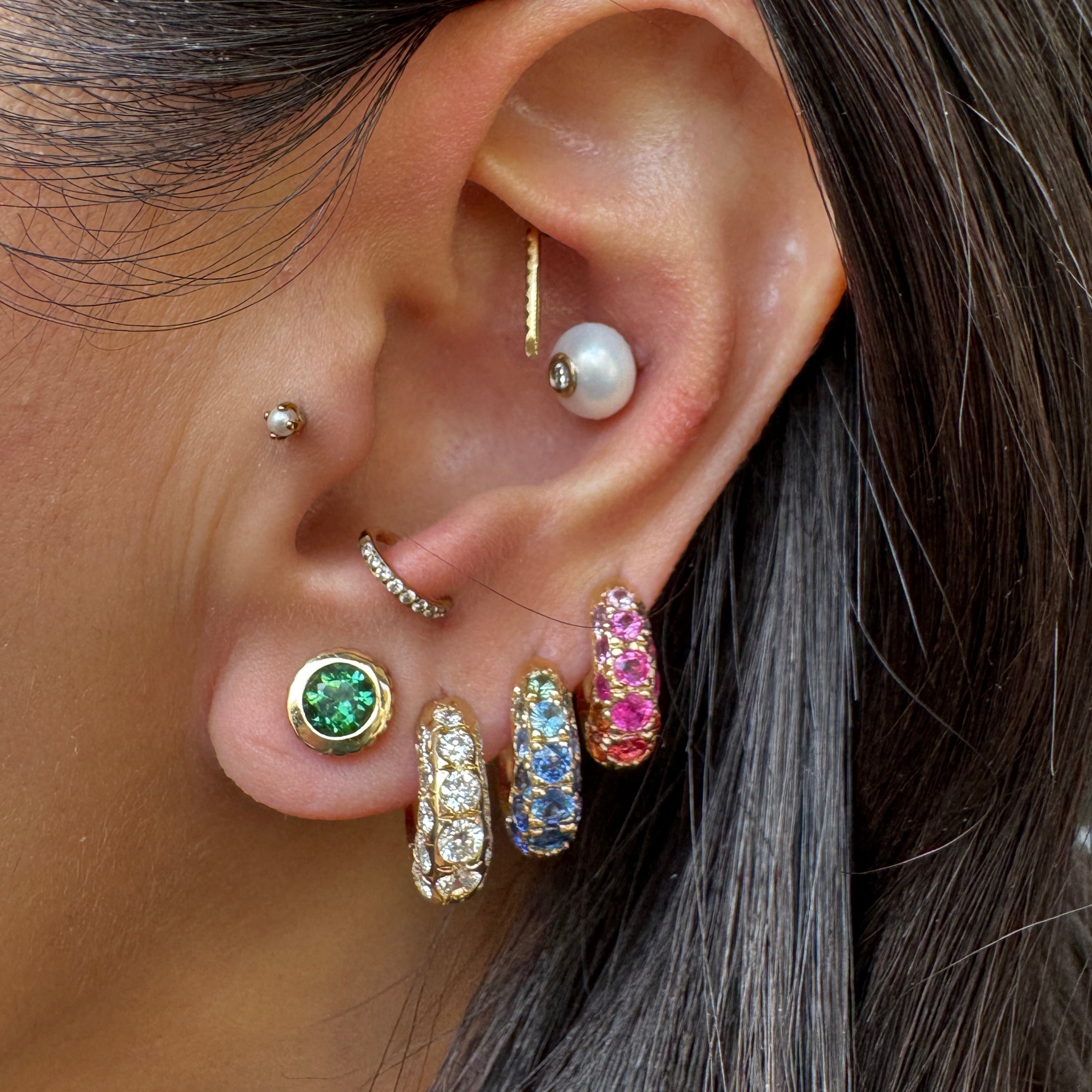 Close-up of an ear with multiple earrings including a pearl, gemstone, and colorful hoop earring.