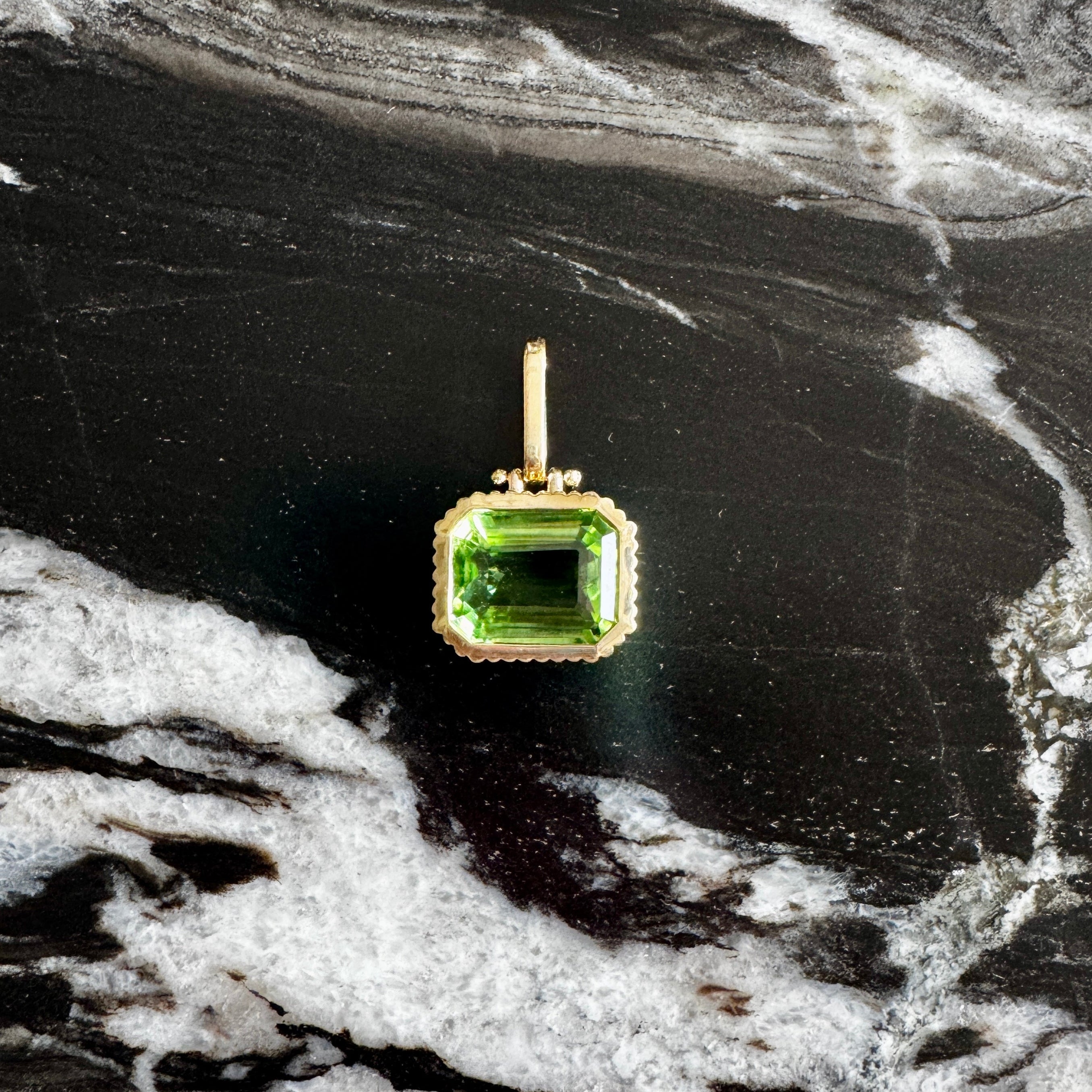 Green gemstone pendant on a gold setting against a marble background