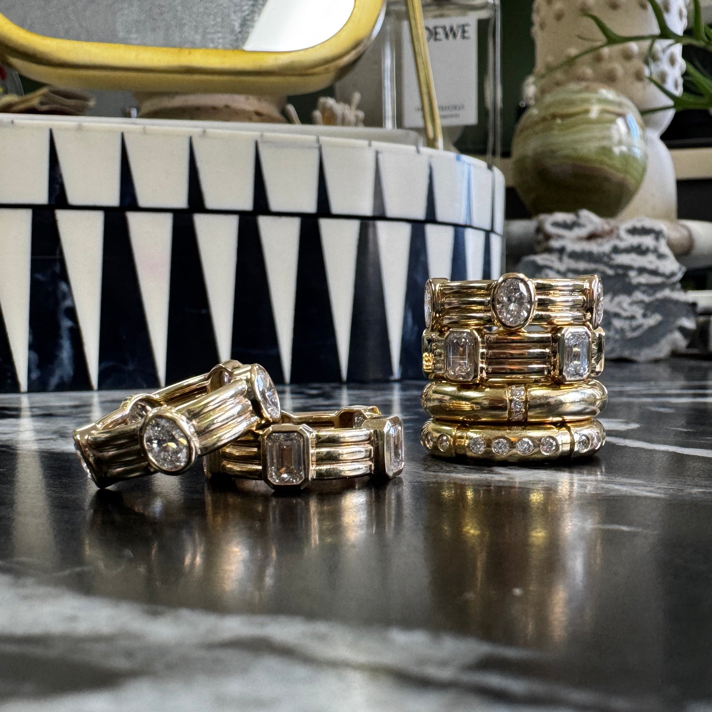 Gold rings with gemstones on a reflective surface with decorative background