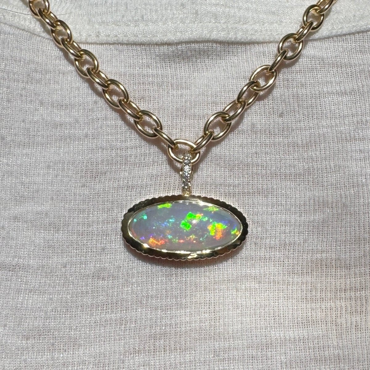 person wearing a gold pendant with a multicolored opal with a diamond bail on a gold chain against a white top