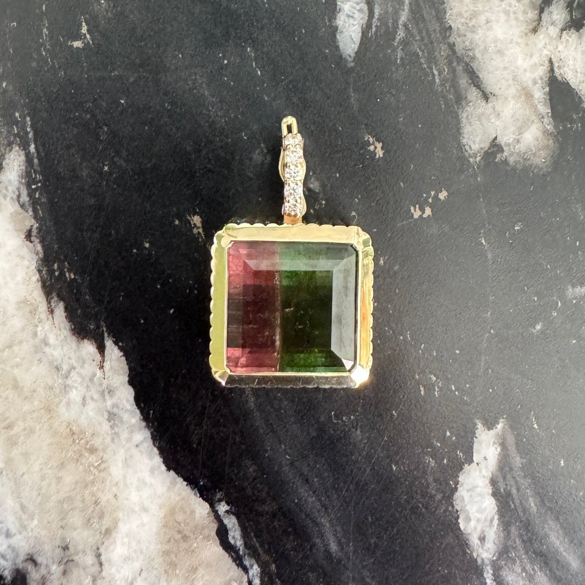 Gold pendant with an emerald-cut watermelon tourmaline and a diamond bail against a black and white marble background