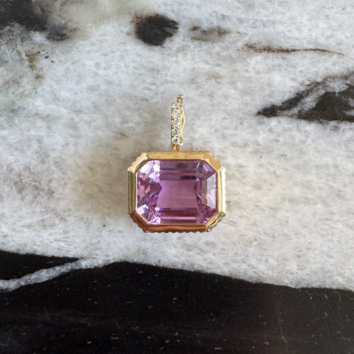Gold pendant with an emerald-cut purple kunzite and a diamond bail against a black and white  marble background