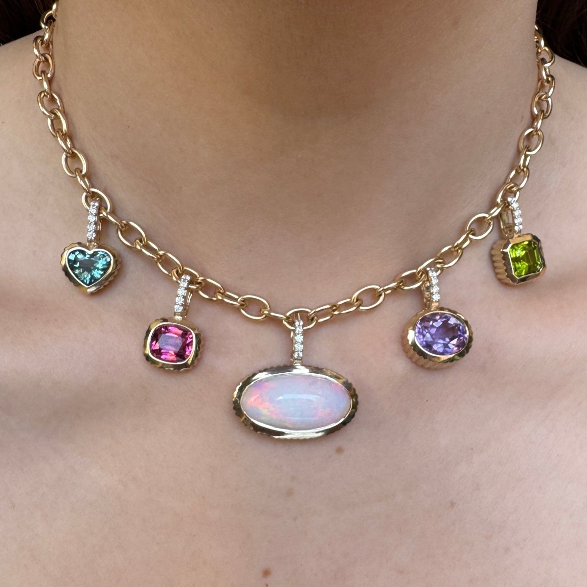 Person wearing a gold chain with multiple gold and multicolored gemstone pendants 