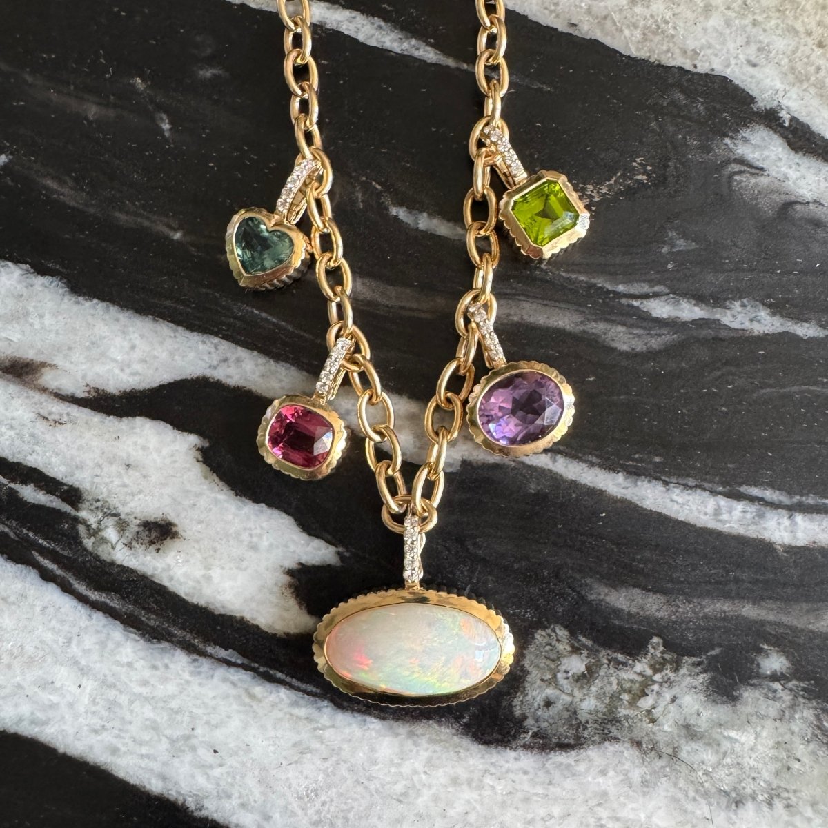 Gold chain with multiple gold and multicolored gemstone pendants against a black and white marble background