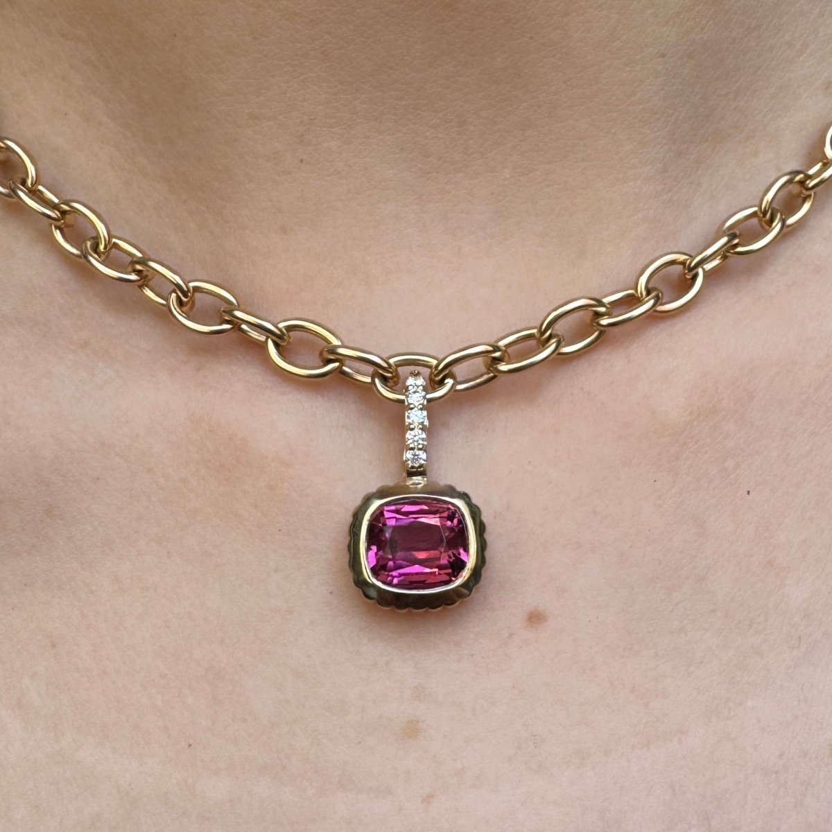 Person wearing a gold pendant with a cushion-cut pink tourmaline and a diamond bail on a gold chain