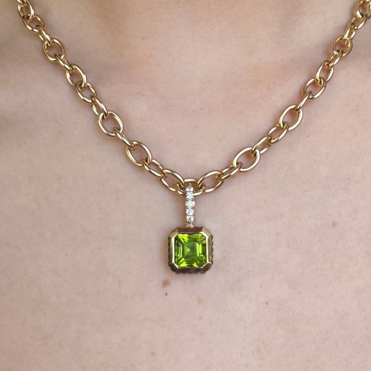 Person wearing a Gold pendant with a square-cut green peridot and a diamond bail on a gold chain