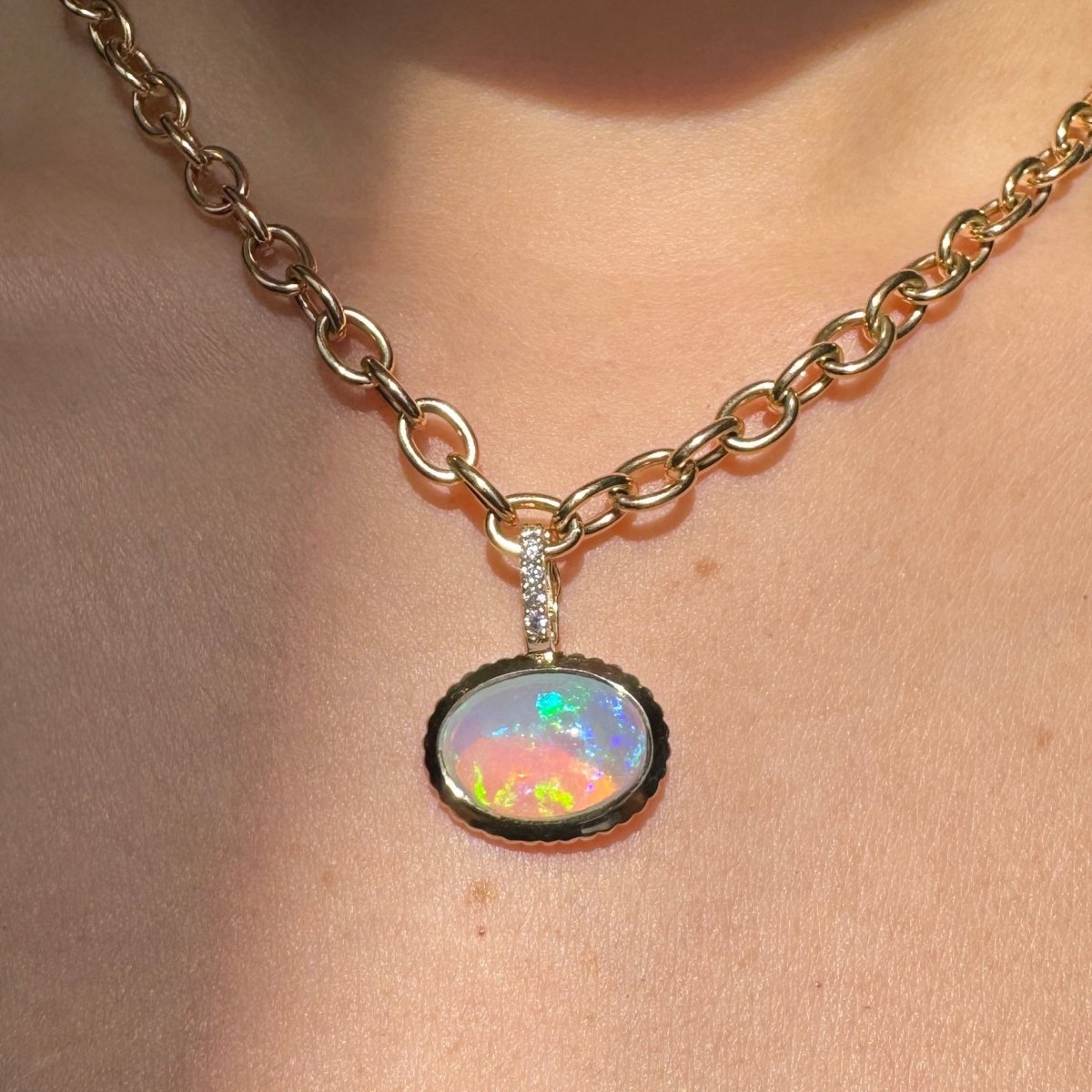 Person wearing a gold pendant with a multicolored opal and a diamond bail on a gold chain 