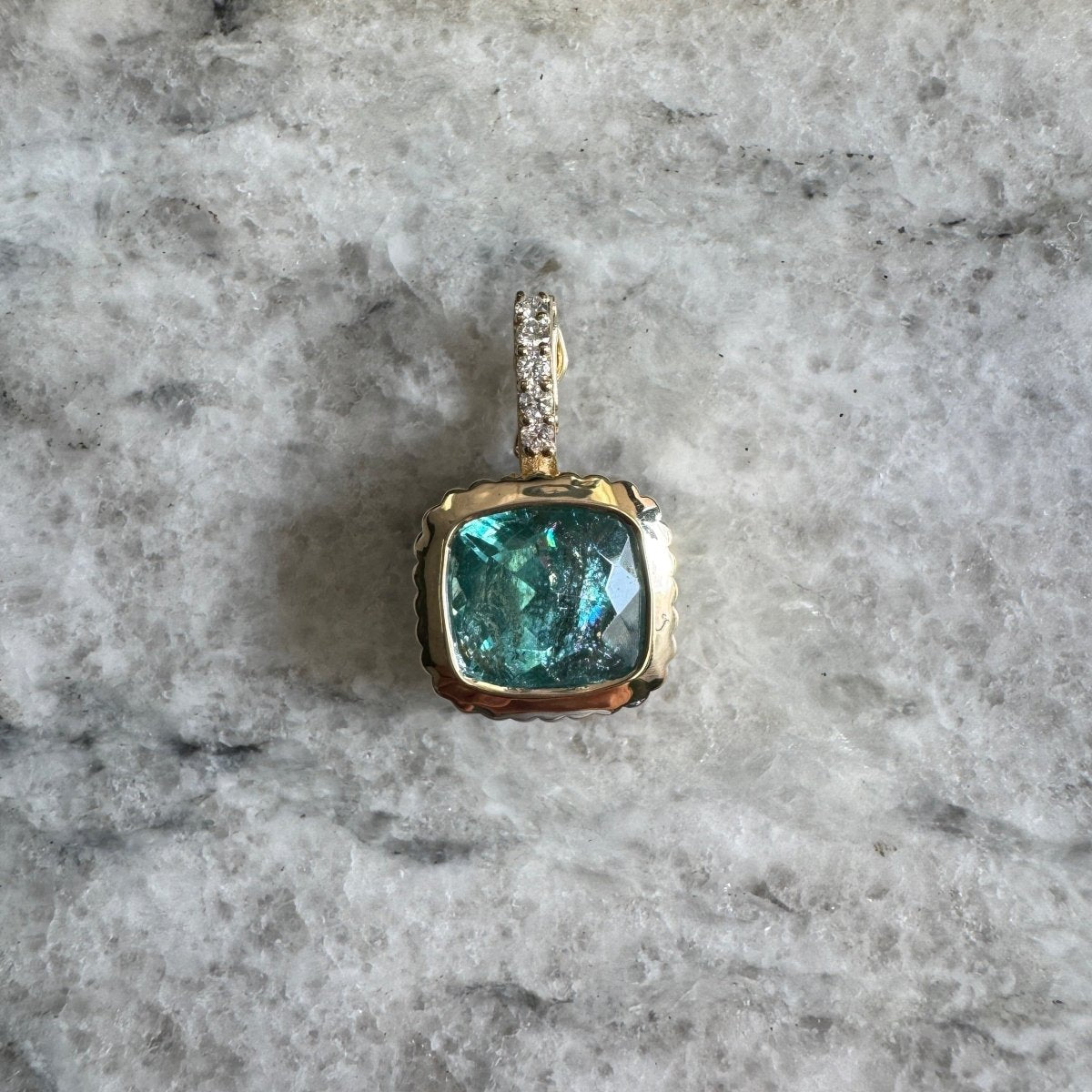 Gold pendant with a blueish green vanadium beryl with a diamond bail against a black and white marble background