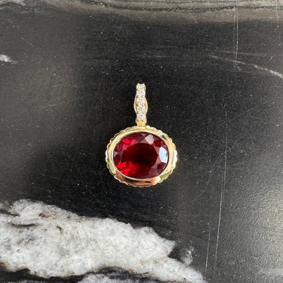Gold pendant with a red sunstone and a diamond bail against a black and white marble background