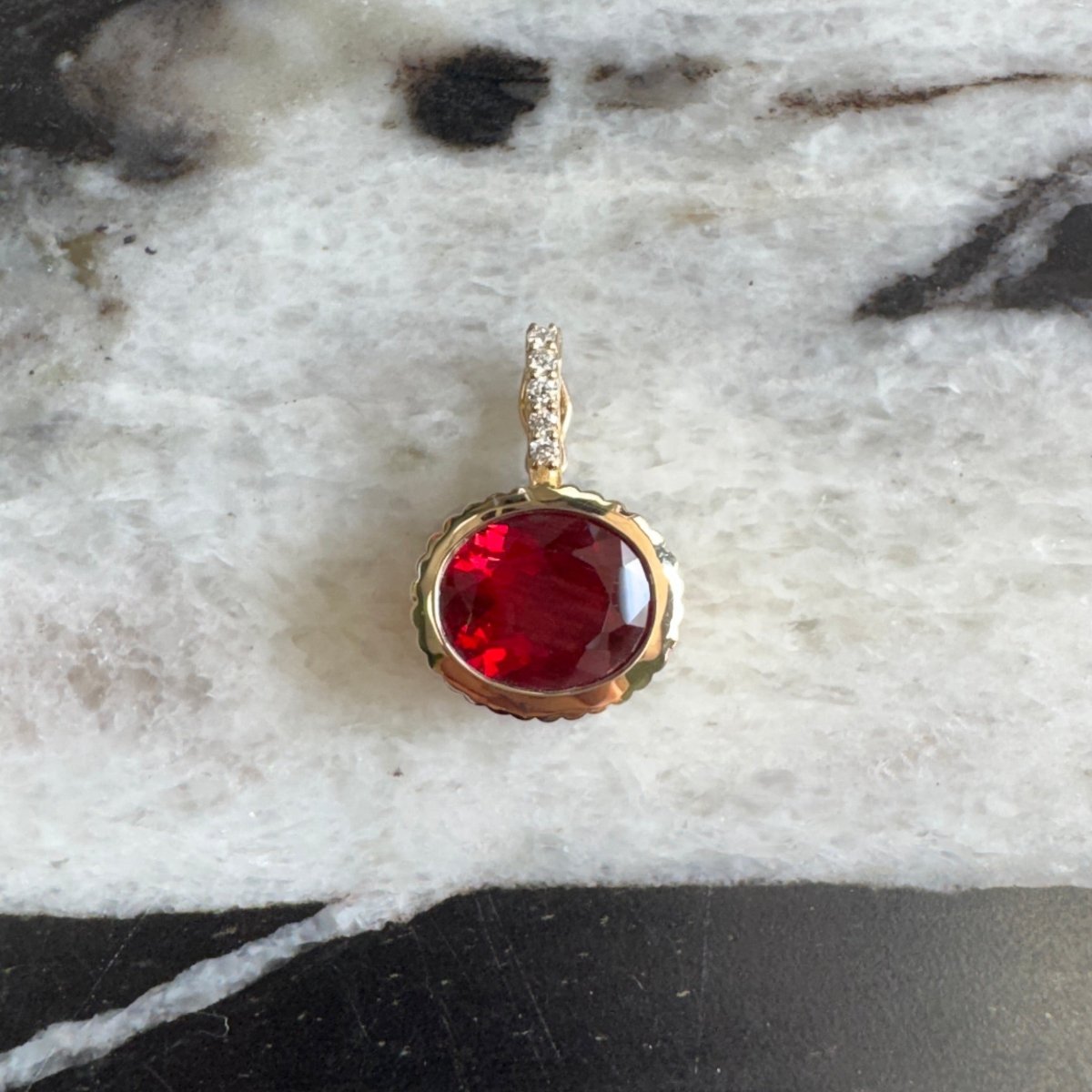 Gold pendant with a red sunstone and a diamond bail against a black and white marble background