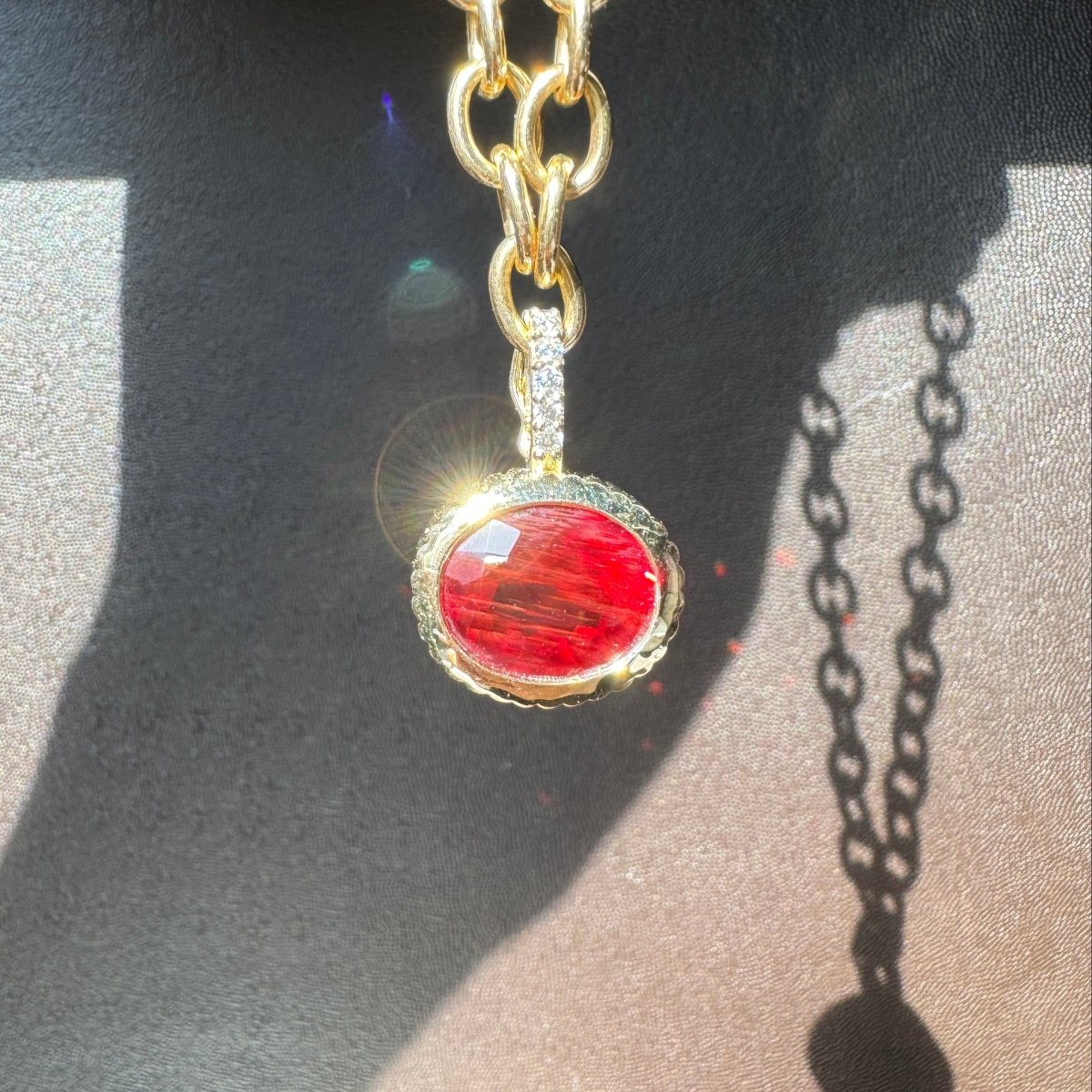 Gold pendant with a red sunstone and a diamond bail on a gold chain against a brown leather background
