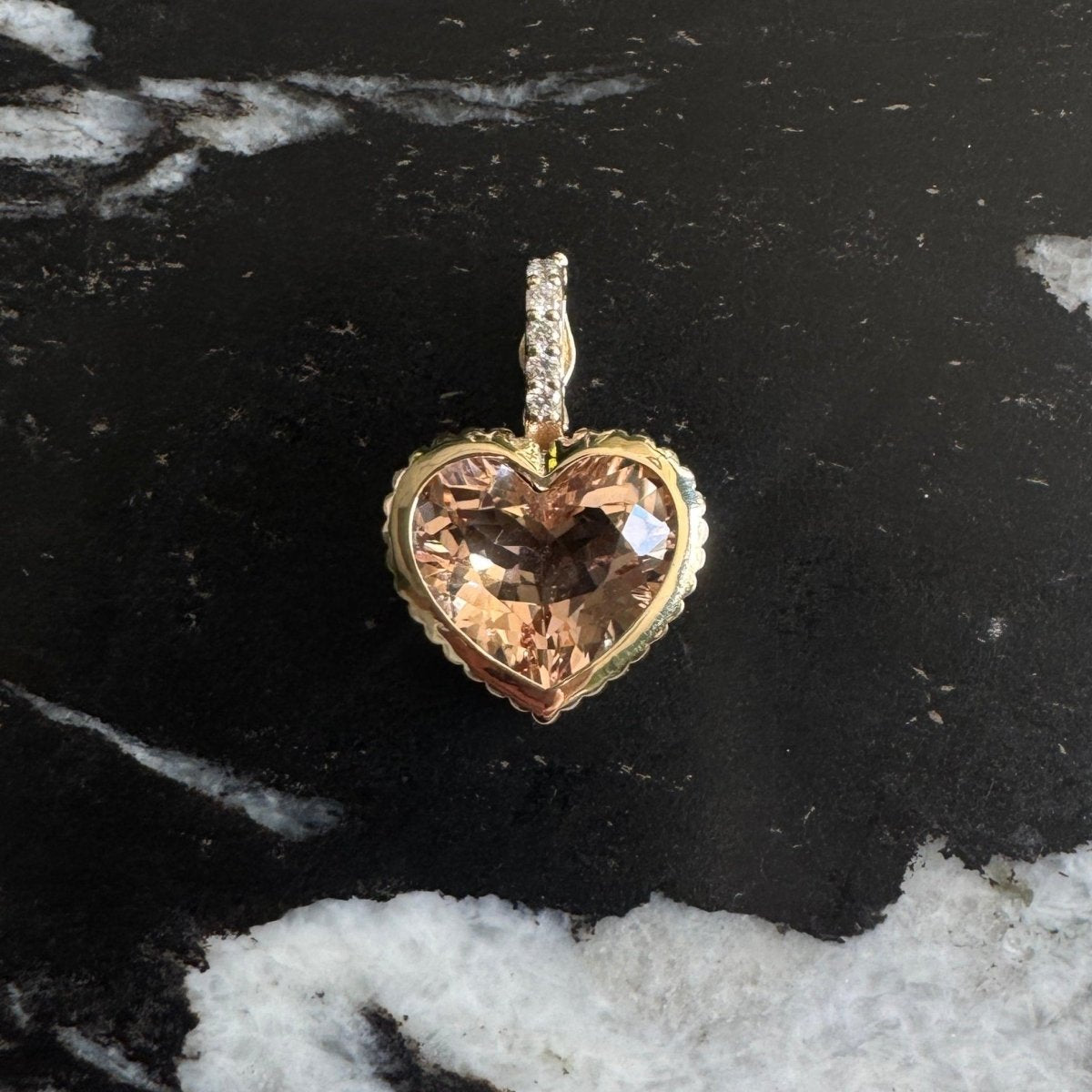 Gold Pendant with a peachy heart-shaped morganite and a diamond bail against a black and white marble background 